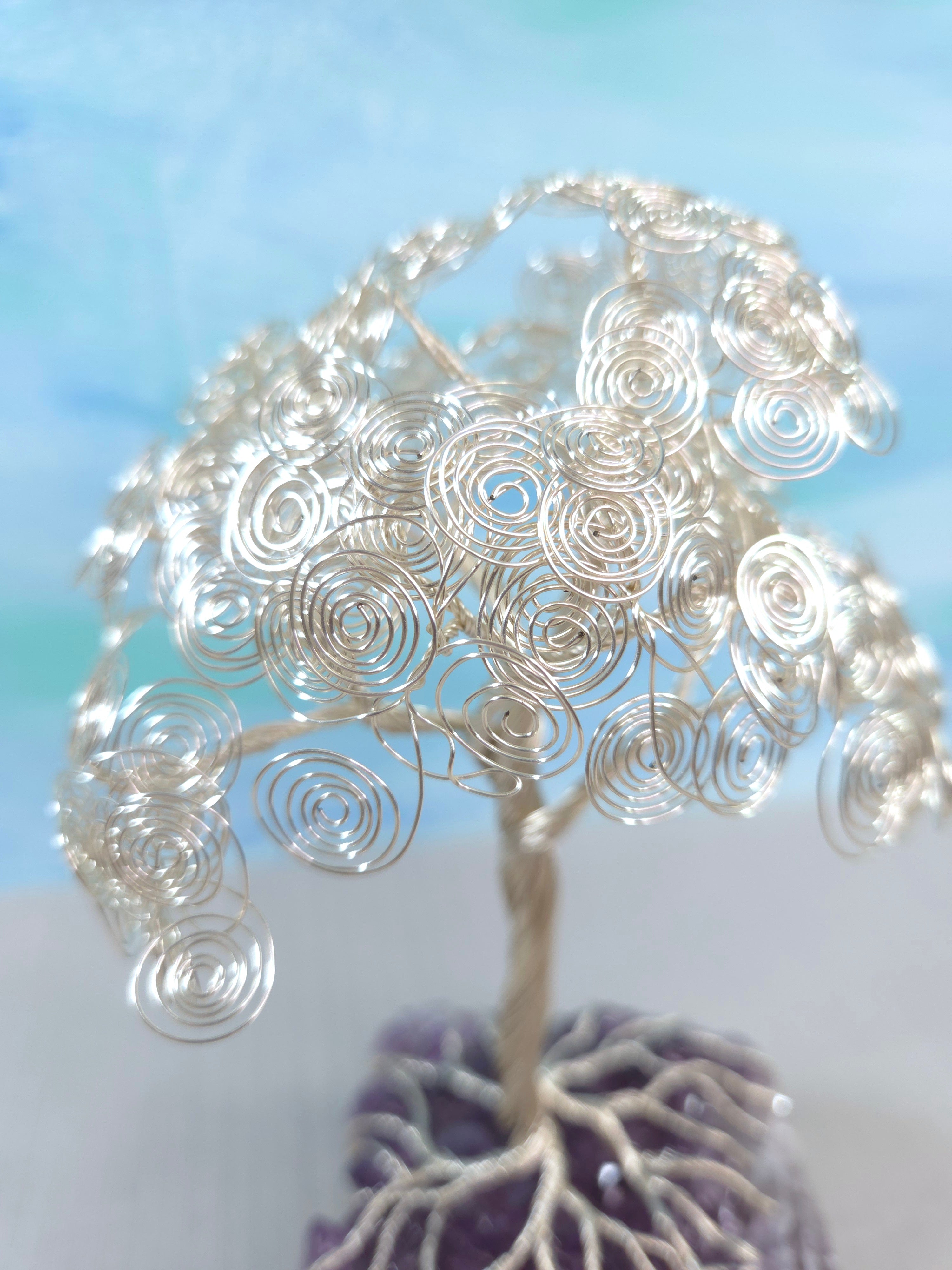 Silver wire tree sculpture with purple base against a light blue background