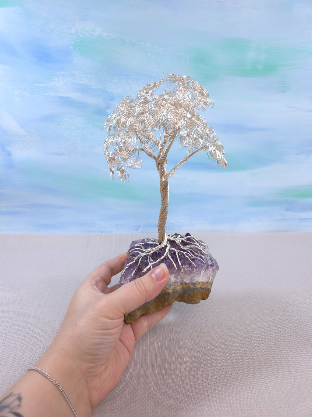 Hand holding a small crystal tree on a rock against a blurred natural background