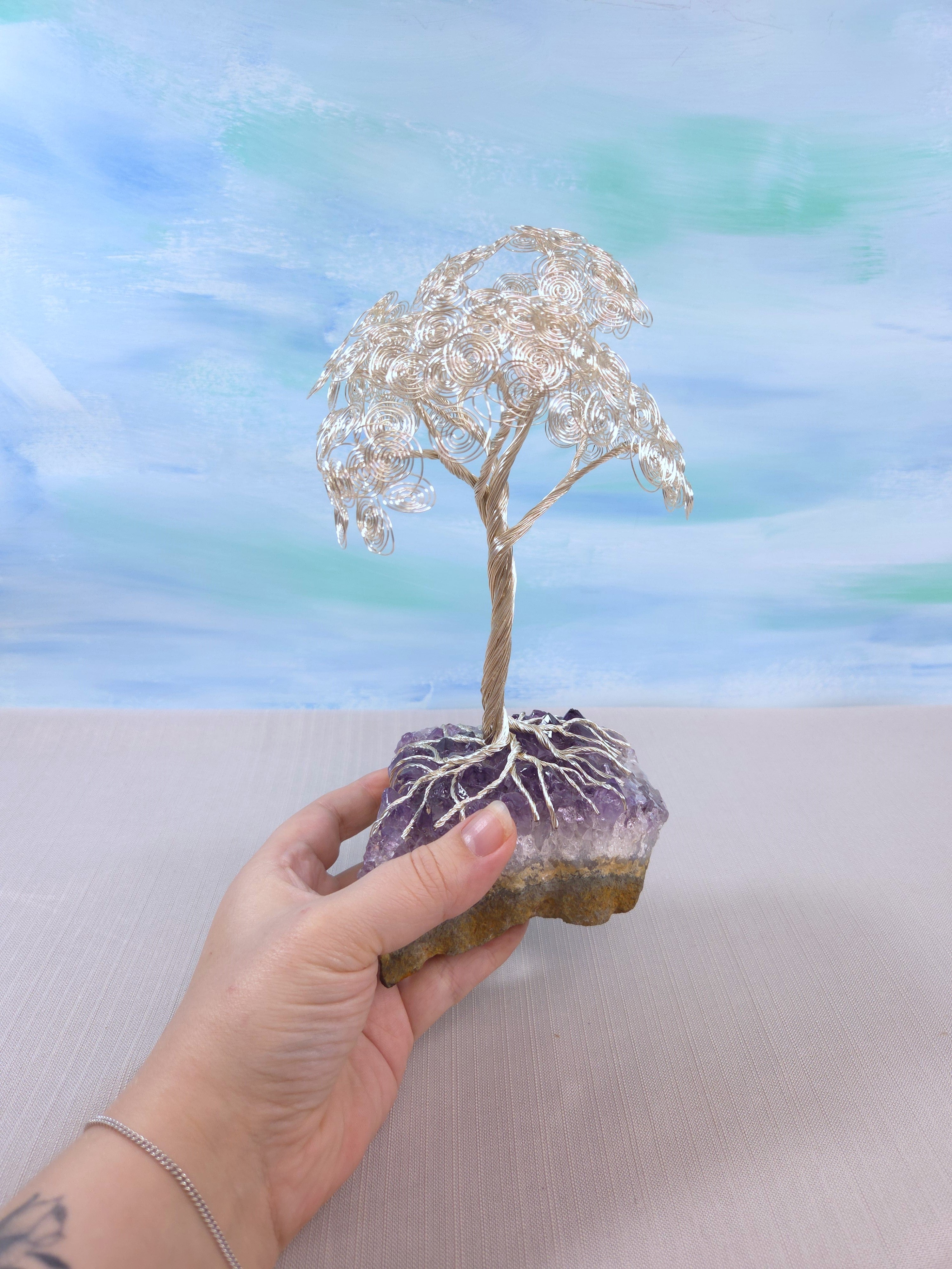 Hand holding a small crystal tree on a rock against a blurred natural background