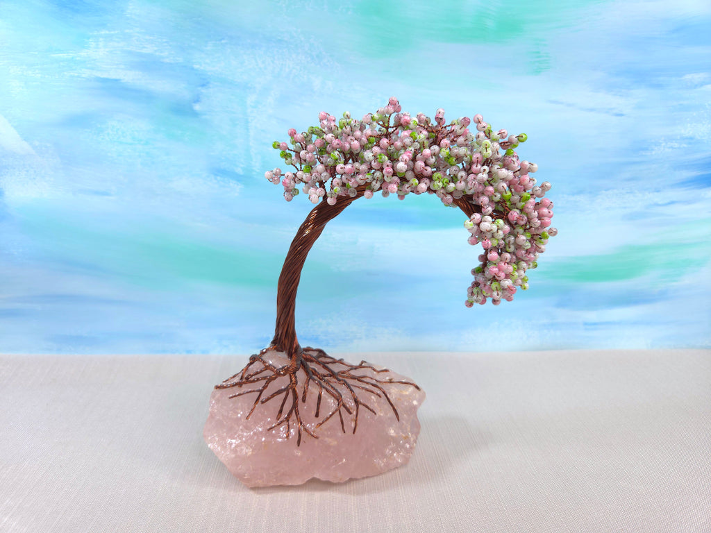 Decorative tree with pink flowers on a rock against a blue and green gradient background