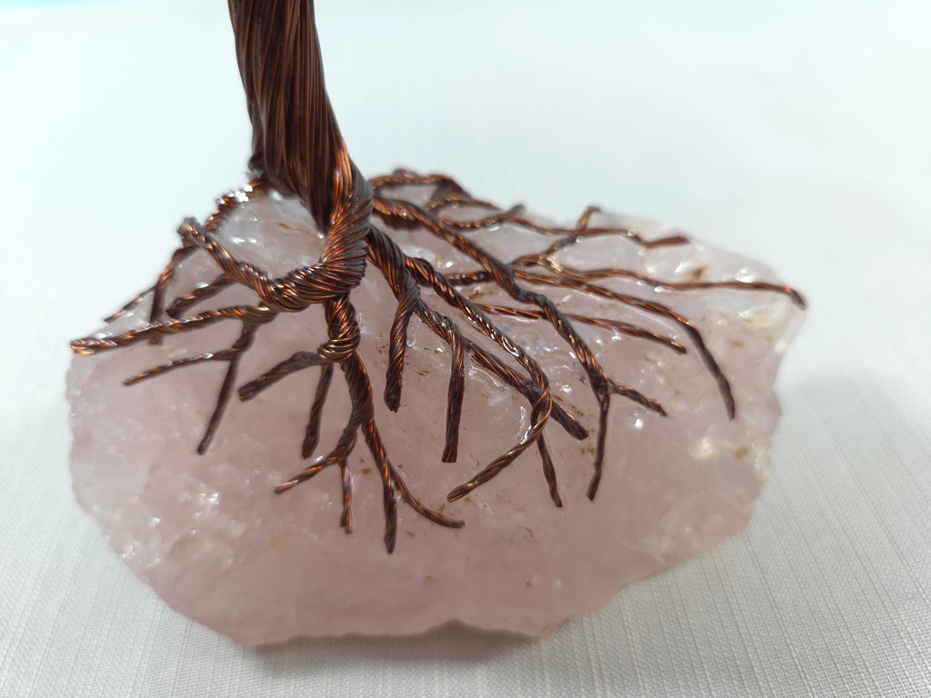 Decorative pendant with wire tree design on a rose quartz stone against a white background