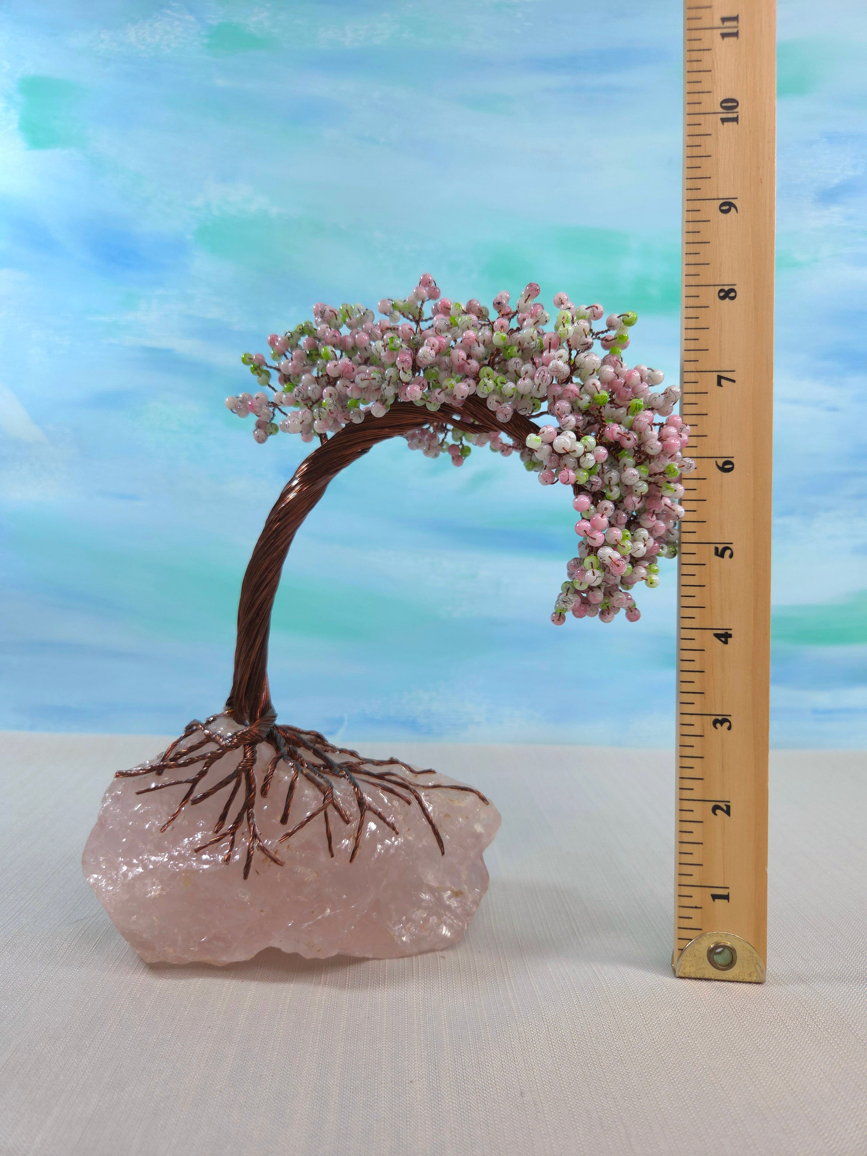 Decorative bonsai tree with pink flowers on a rose quartz base, next to a ruler for scale.