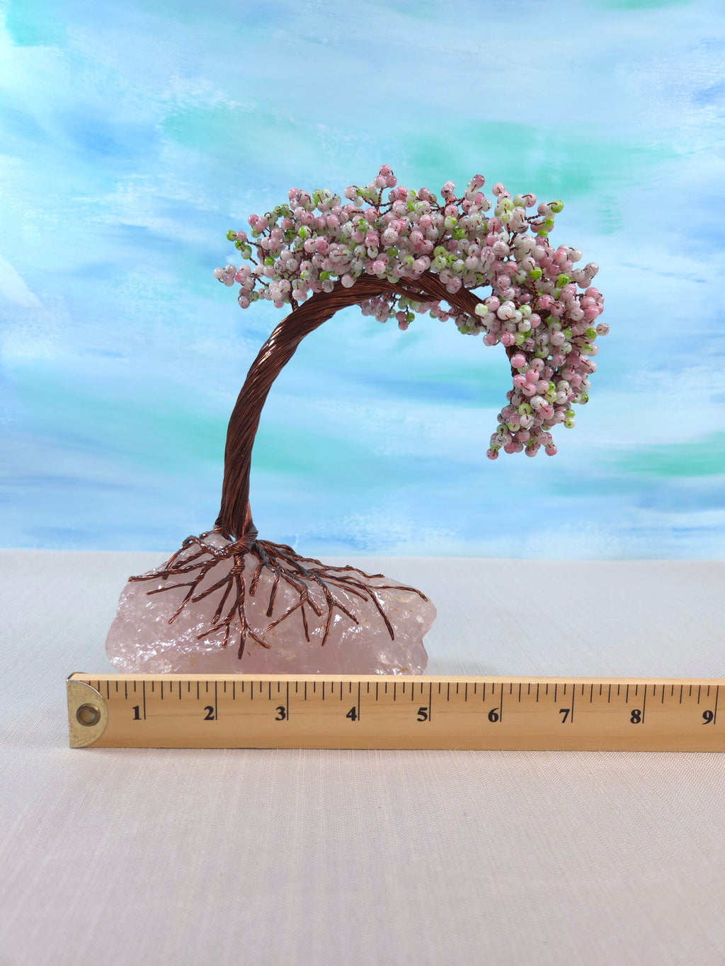 Decorative bonsai tree with pink blossoms on a white surface with a ruler for scale.