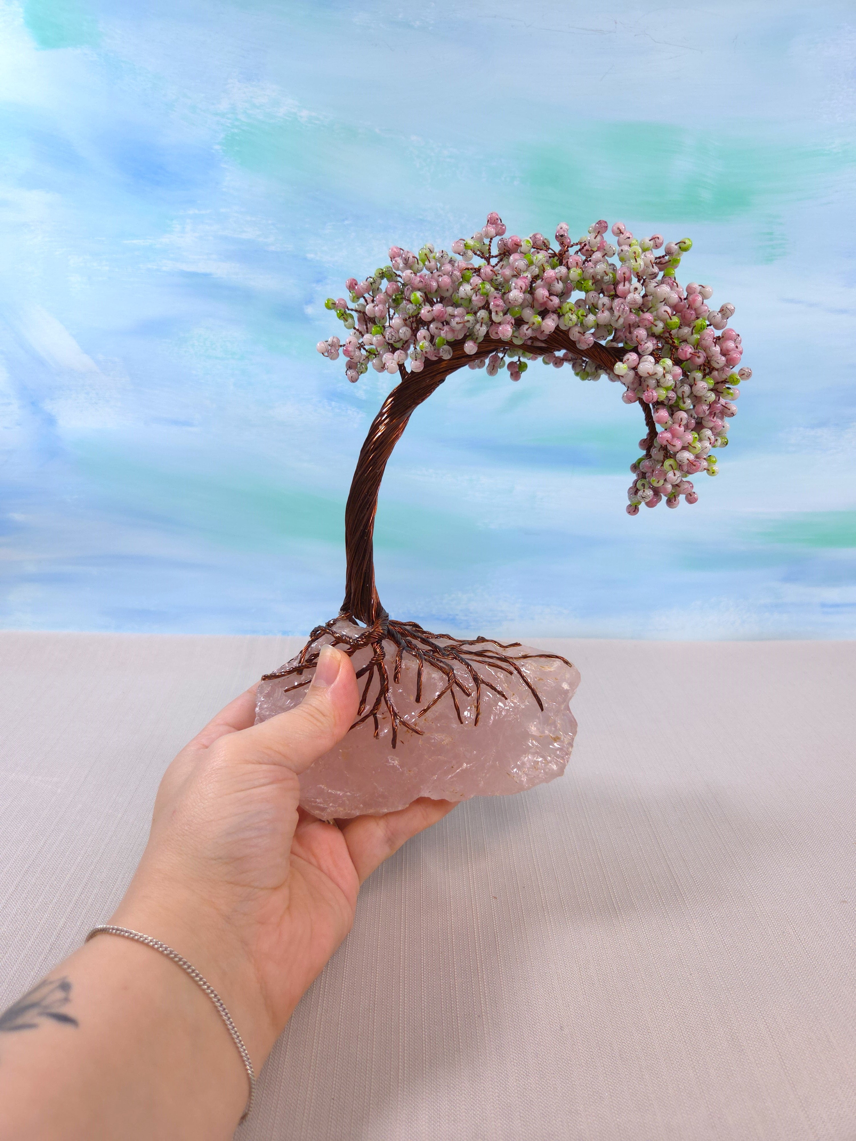 Small bonsai tree with pink flowers held by a hand against a blurred background