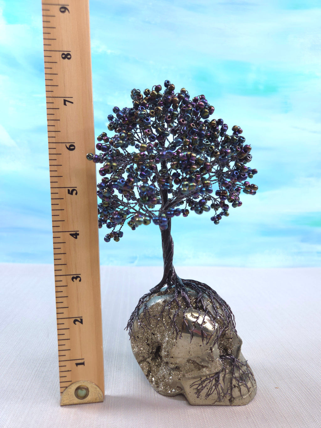 Decorative tree sculpture on a skull with a ruler for scale against a light blue background