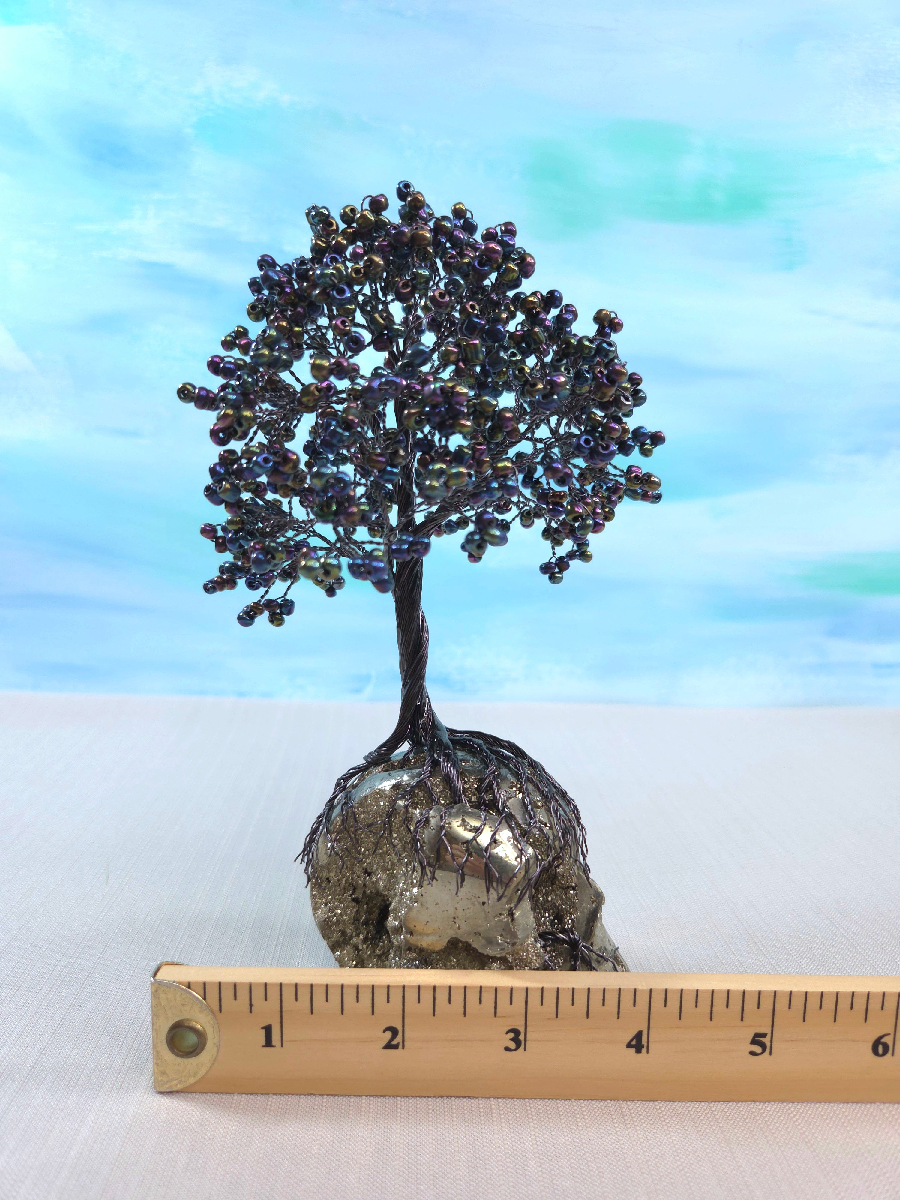 Decorative tree sculpture on a metallic base with a ruler for scale against a blue gradient background