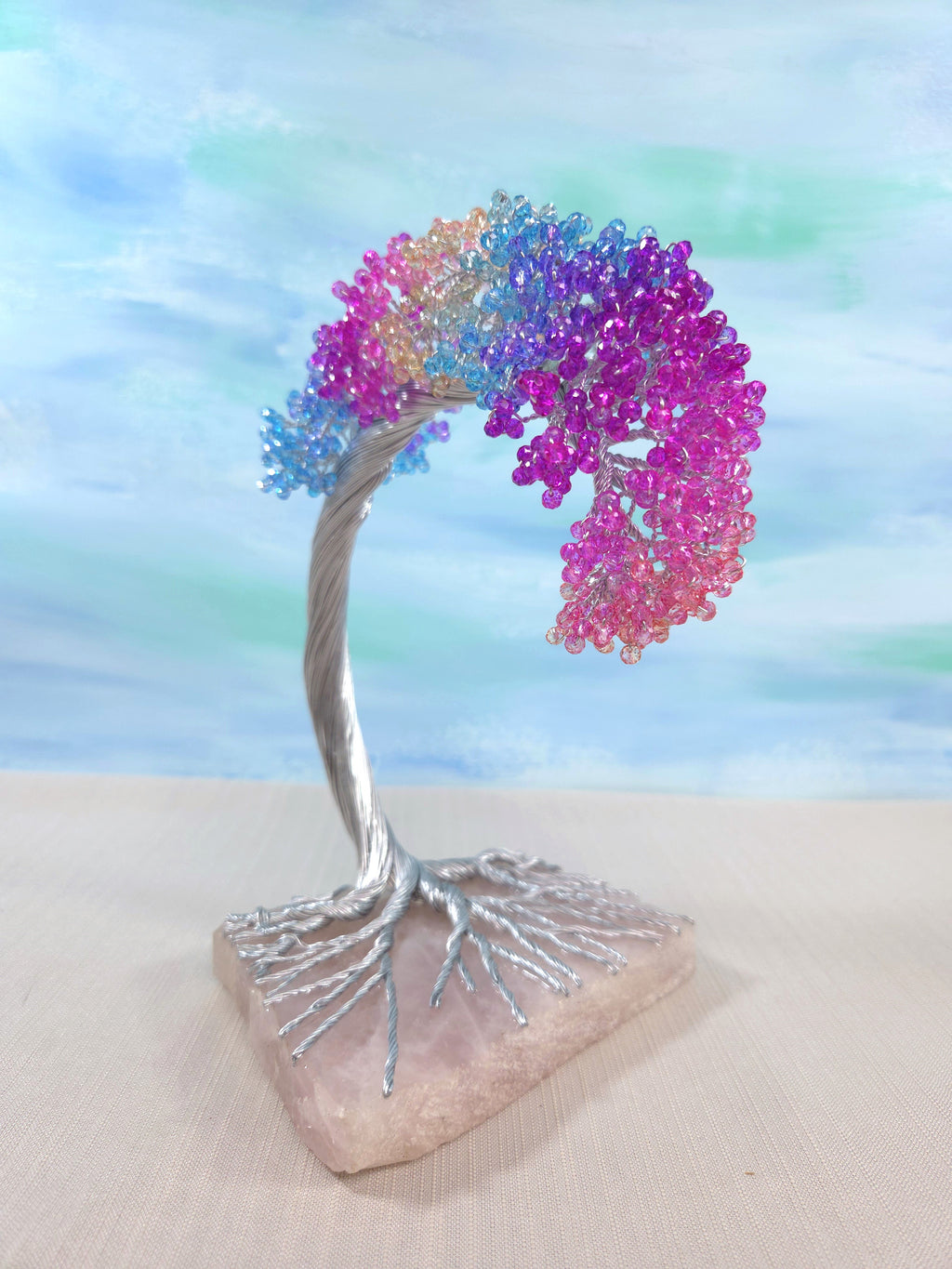 Colorful beaded tree sculpture on a stone base with a pastel gradient background