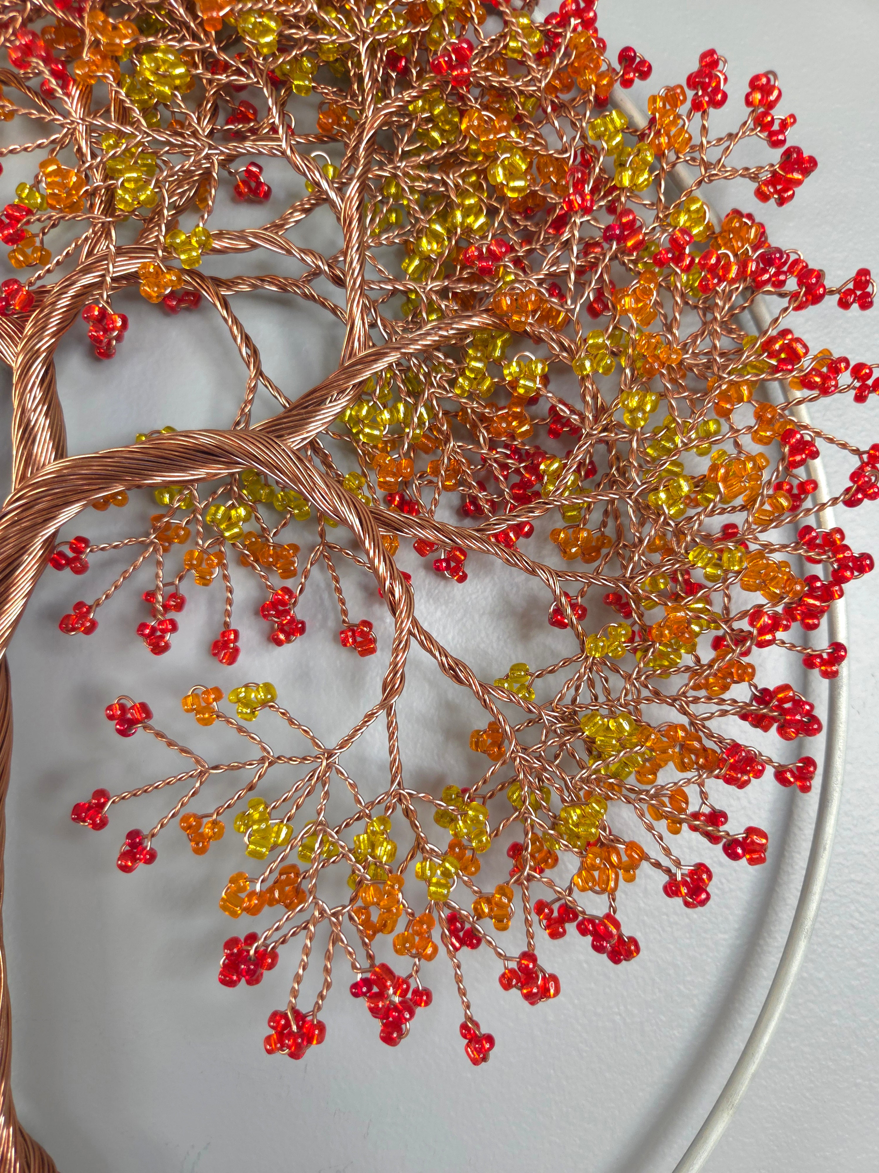 Decorative wall art with a tree design made of copper wire and colored beads on a gray background.
