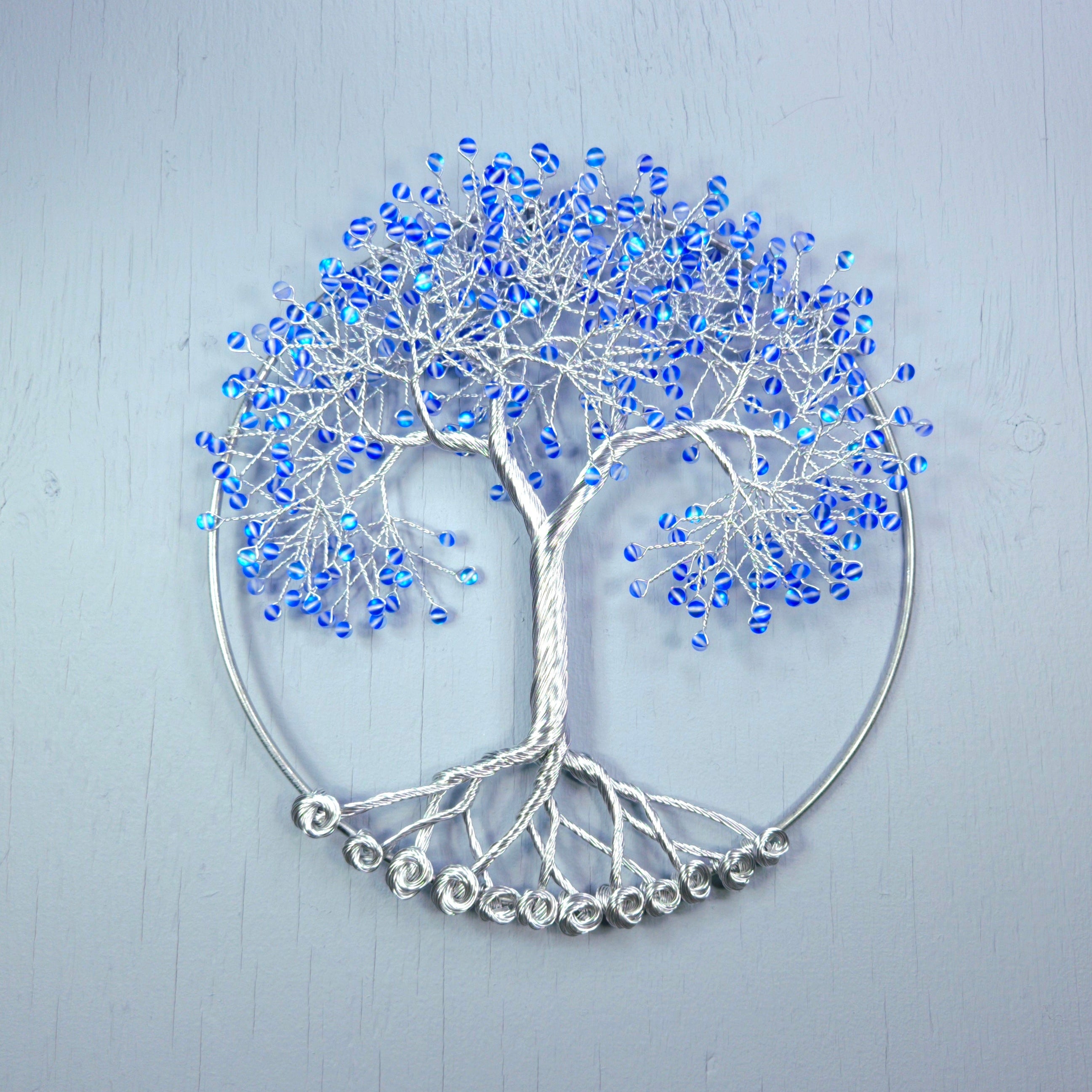 Decorative wall art of a tree with blue beads on a light gray background