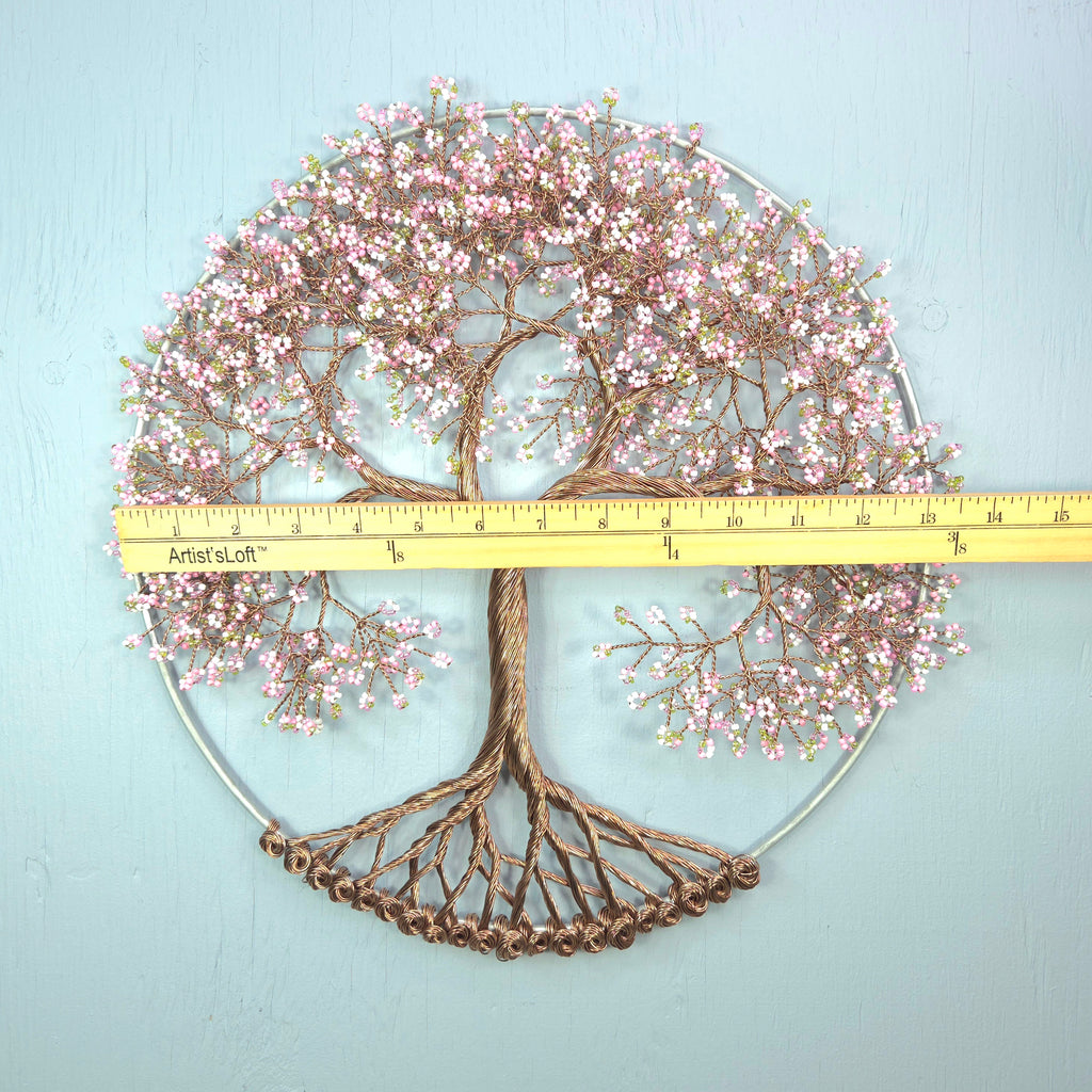 Decorative wall art of a tree with pink blossoms and a ruler for scale on a light blue background