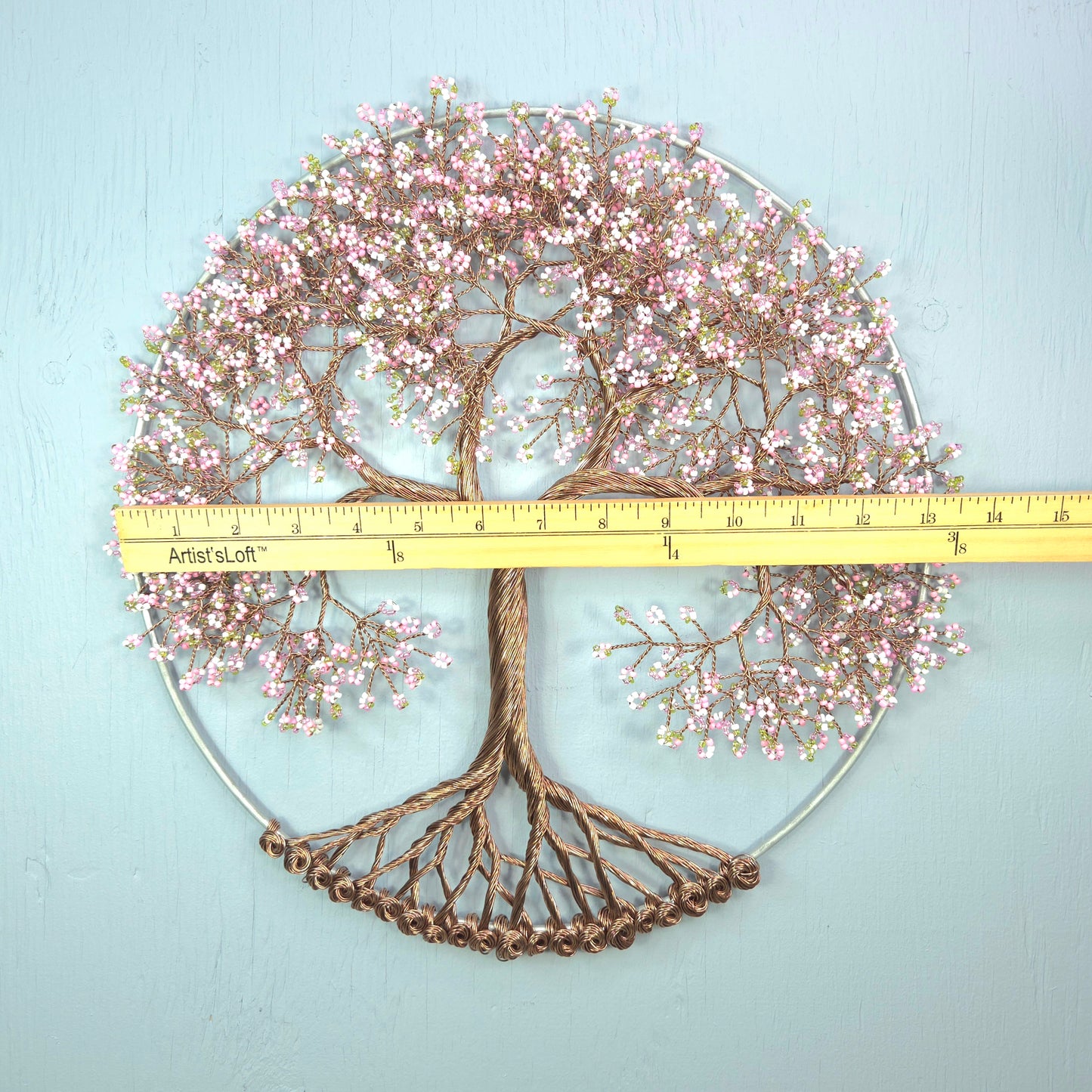 Decorative wall art of a tree with pink blossoms and a ruler for scale on a light blue background