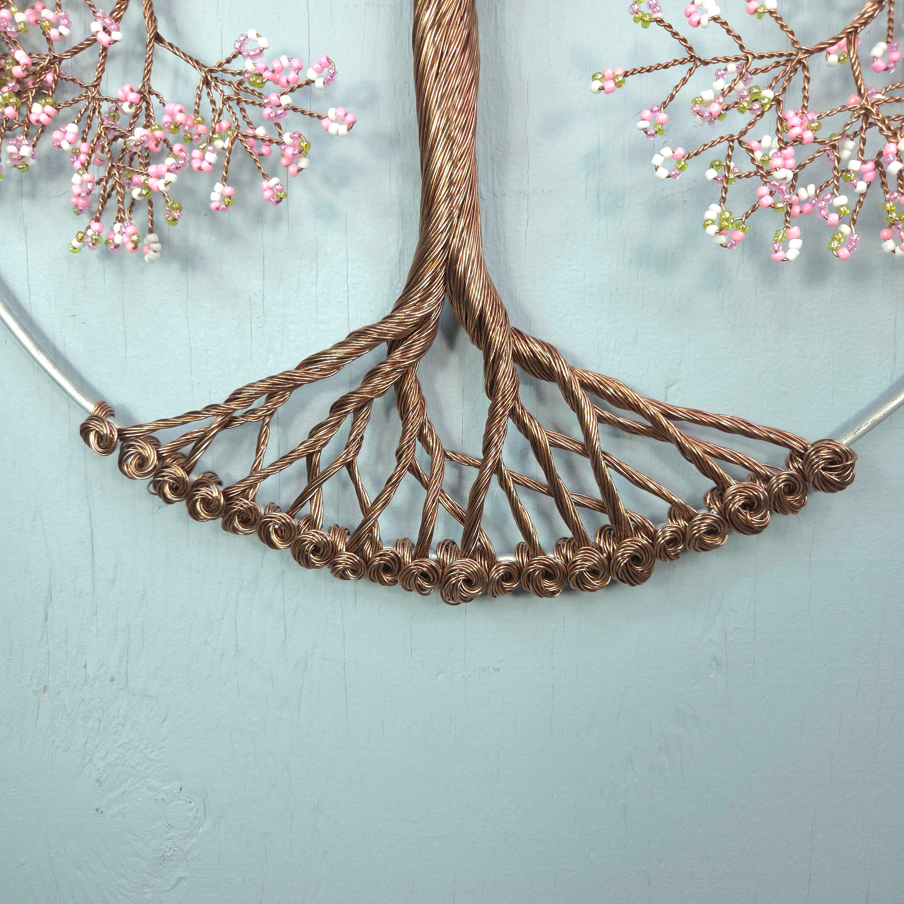 Decorative wall piece with braided brown wire and pink floral branches on a light blue background