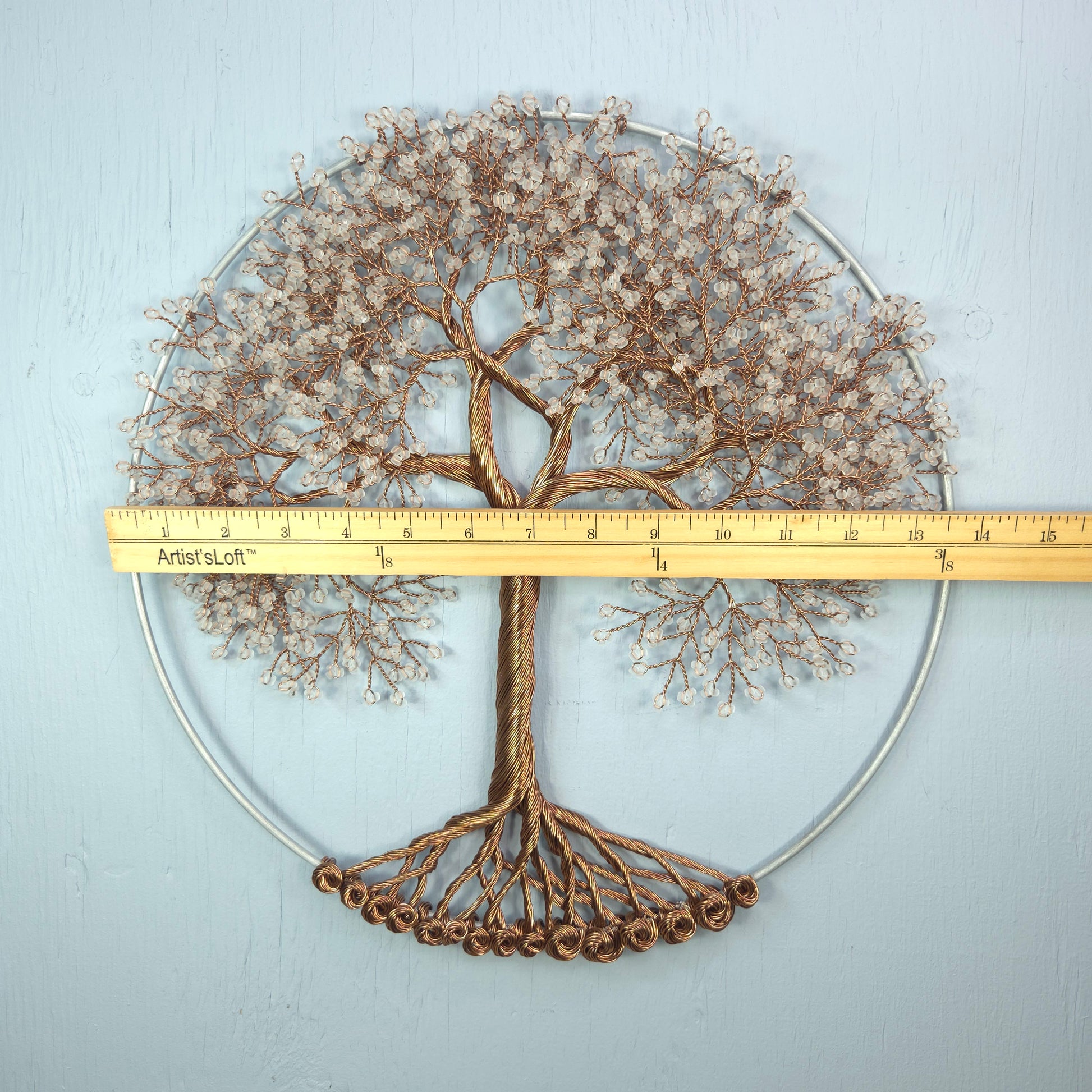 Decorative metal tree wall art with a ruler for scale on a light gray background