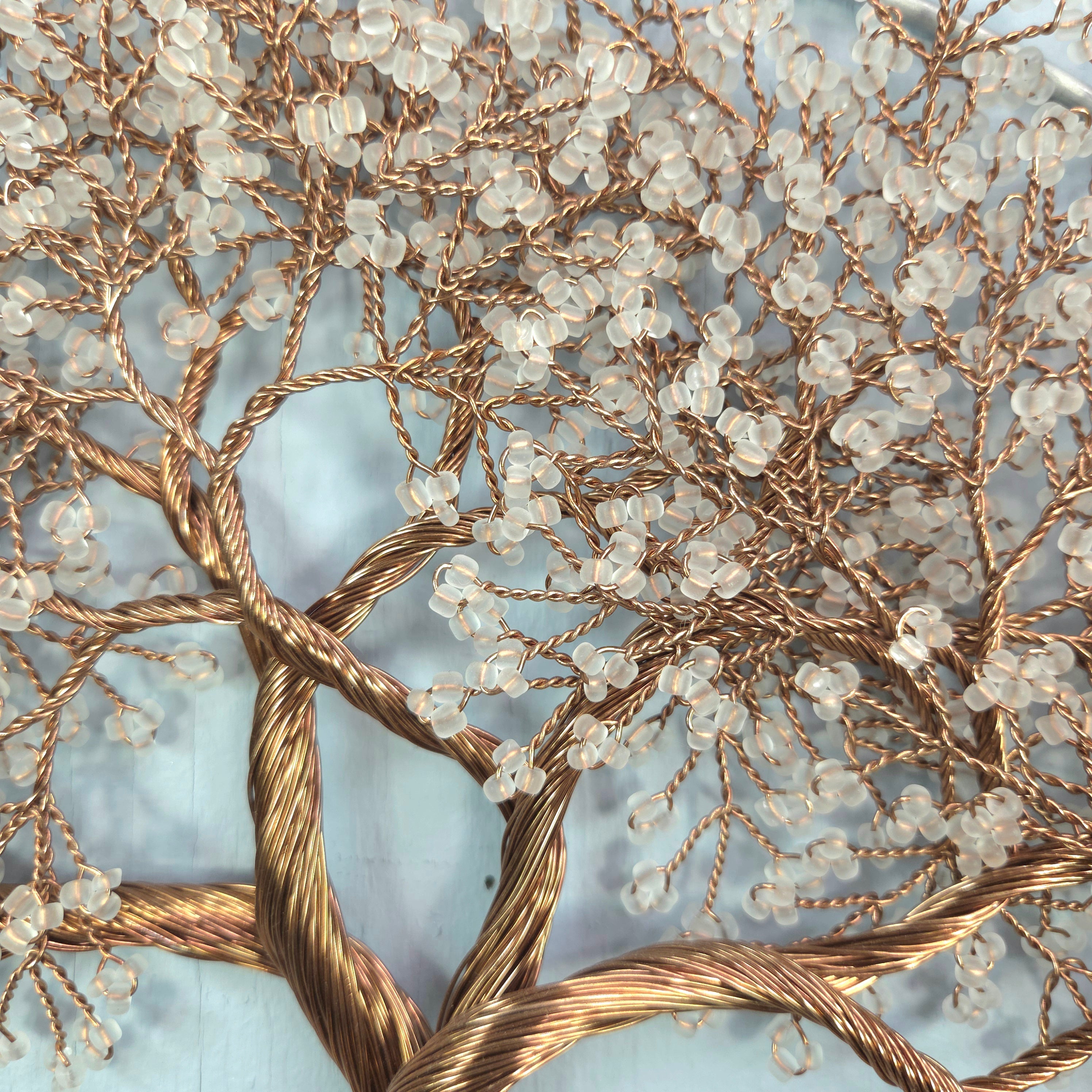 Decorative wall art with intertwined branches and small beads on a light blue background