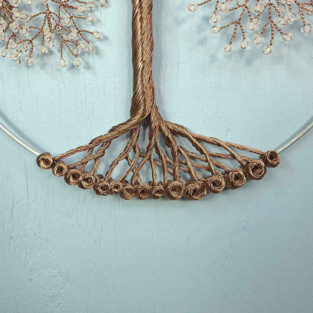 Close-up of a decorative wreath with brown wire and white beads on a light blue background