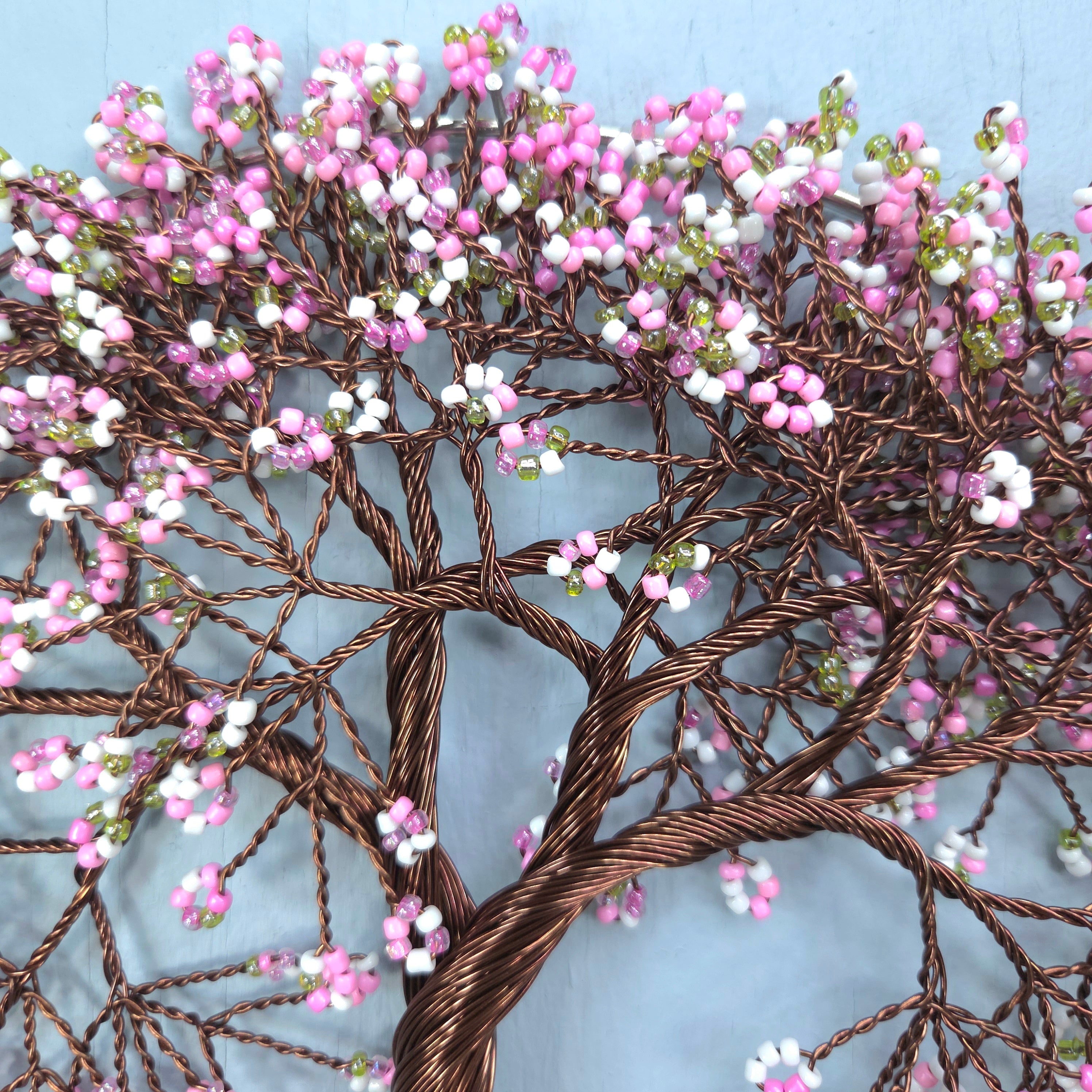Decorative wire tree sculpture with pink and white beads against a light blue background