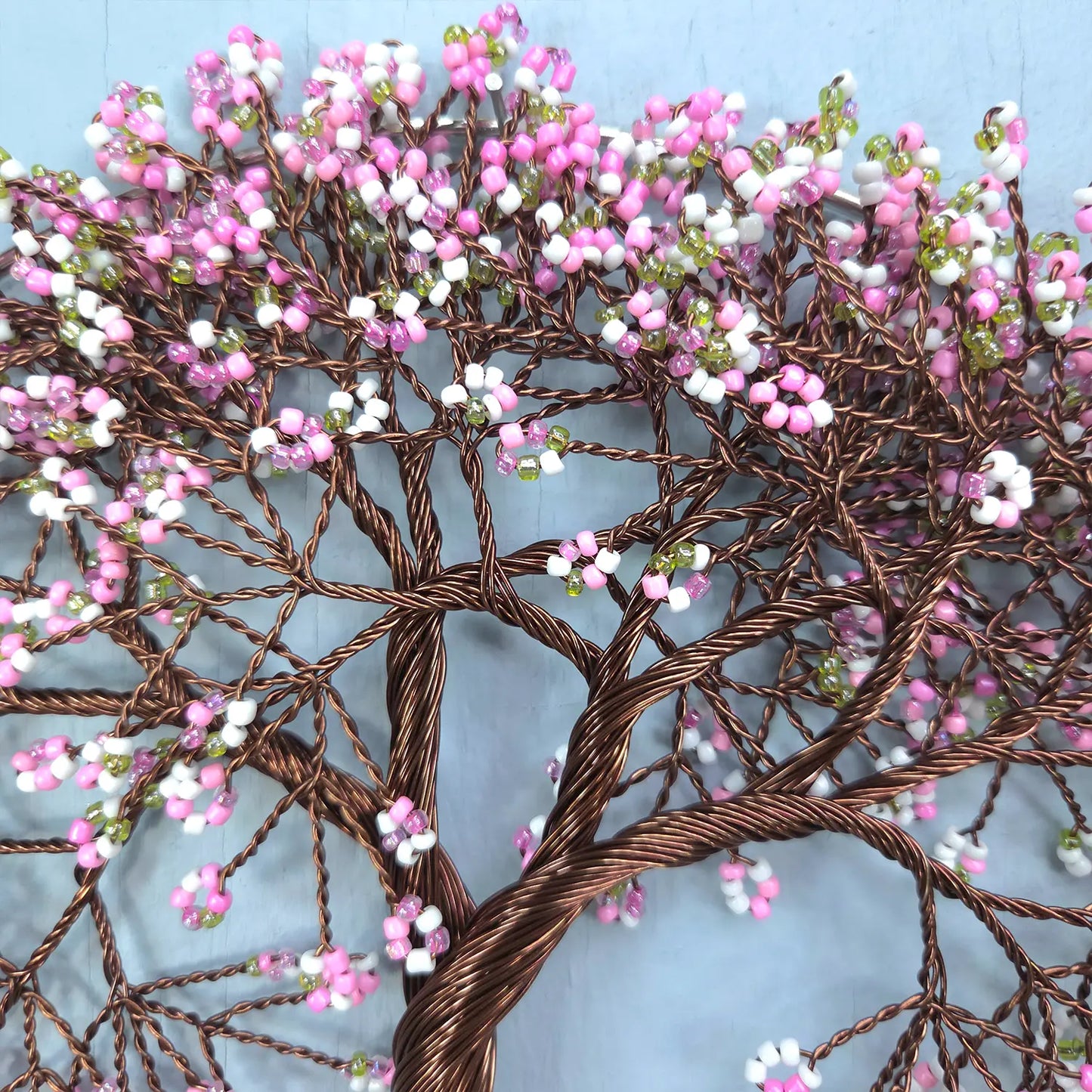 Decorative wire tree with pink and white beads against a light blue background