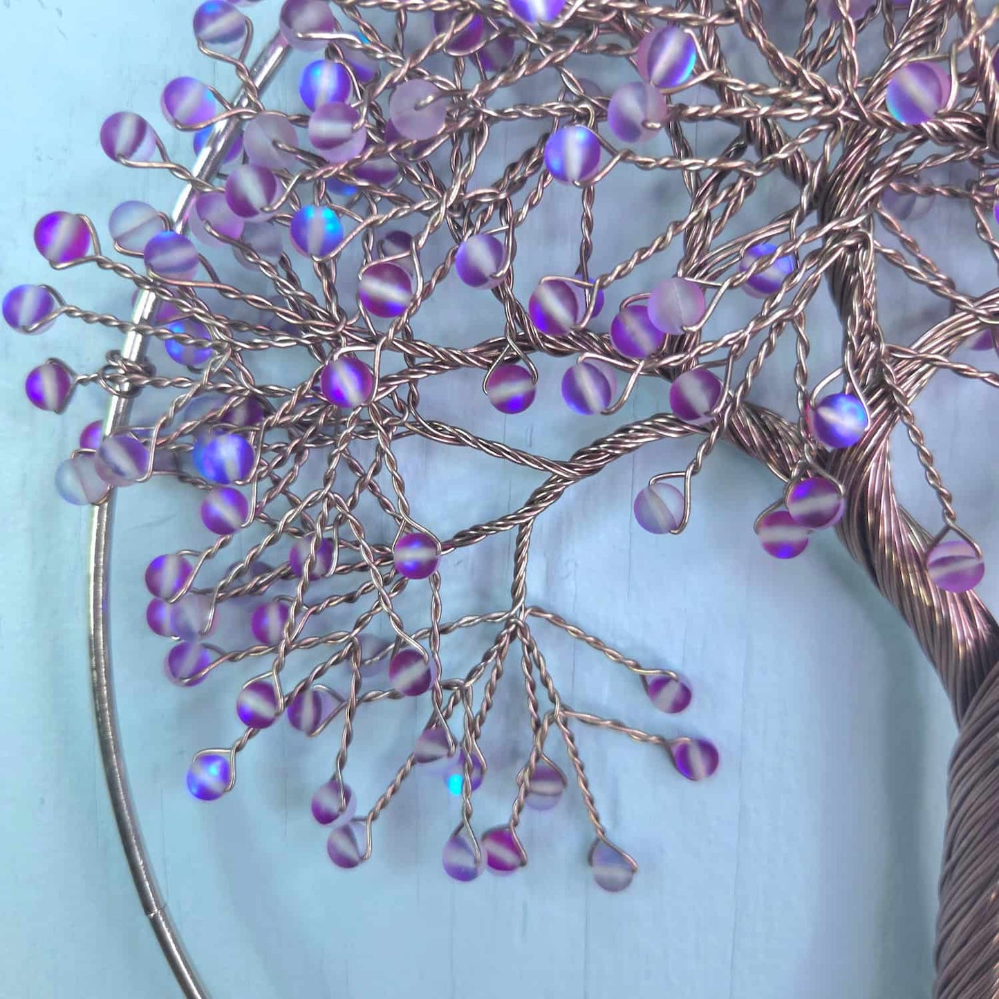 A close-up of a decorative wire tree branch arrangement with iridescent purple and blue bead-like accents, set against a light blue background.