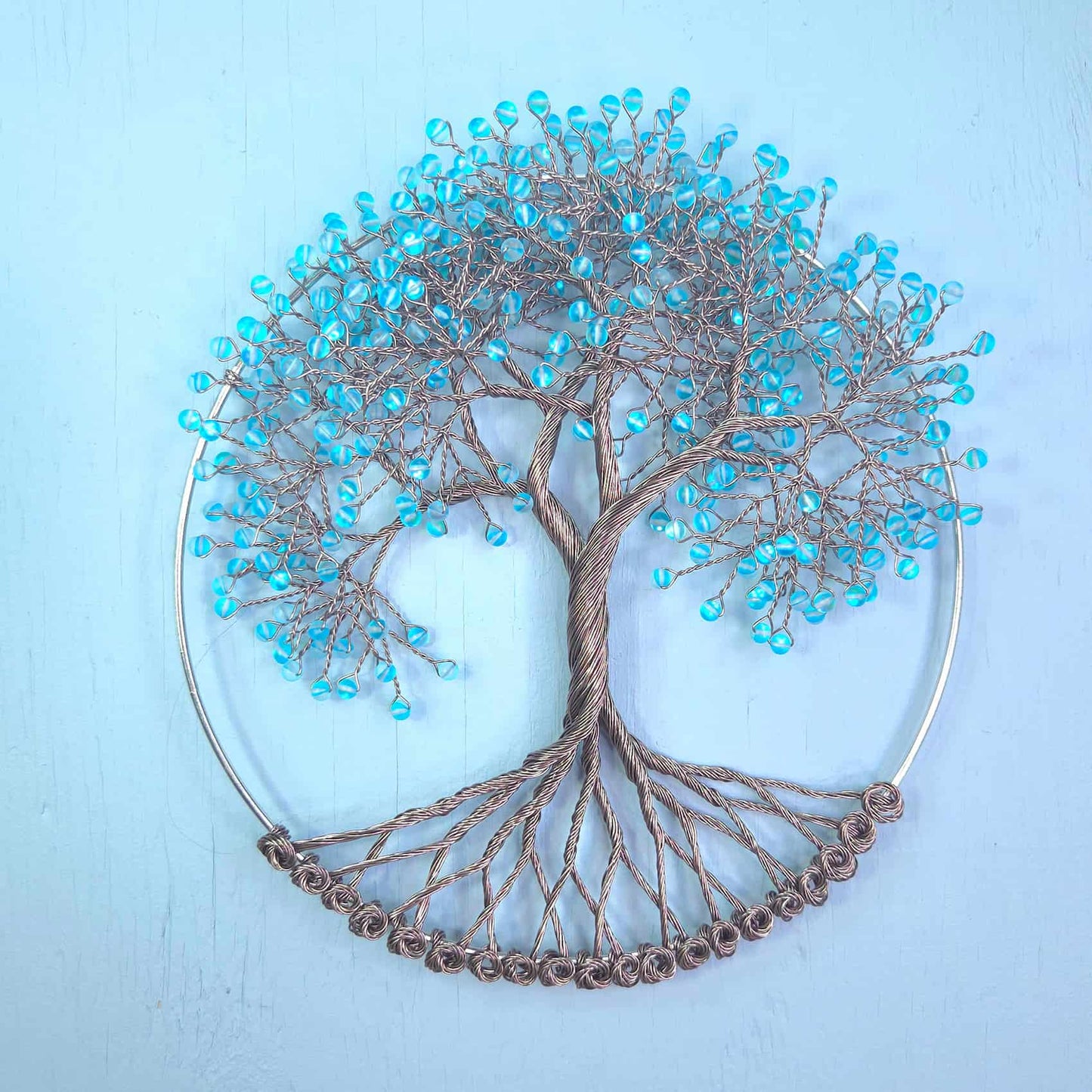 Wire tree of life wall art with turquoise blue seed beads on branches, mounted on a circular metal hoop against a light blue background.