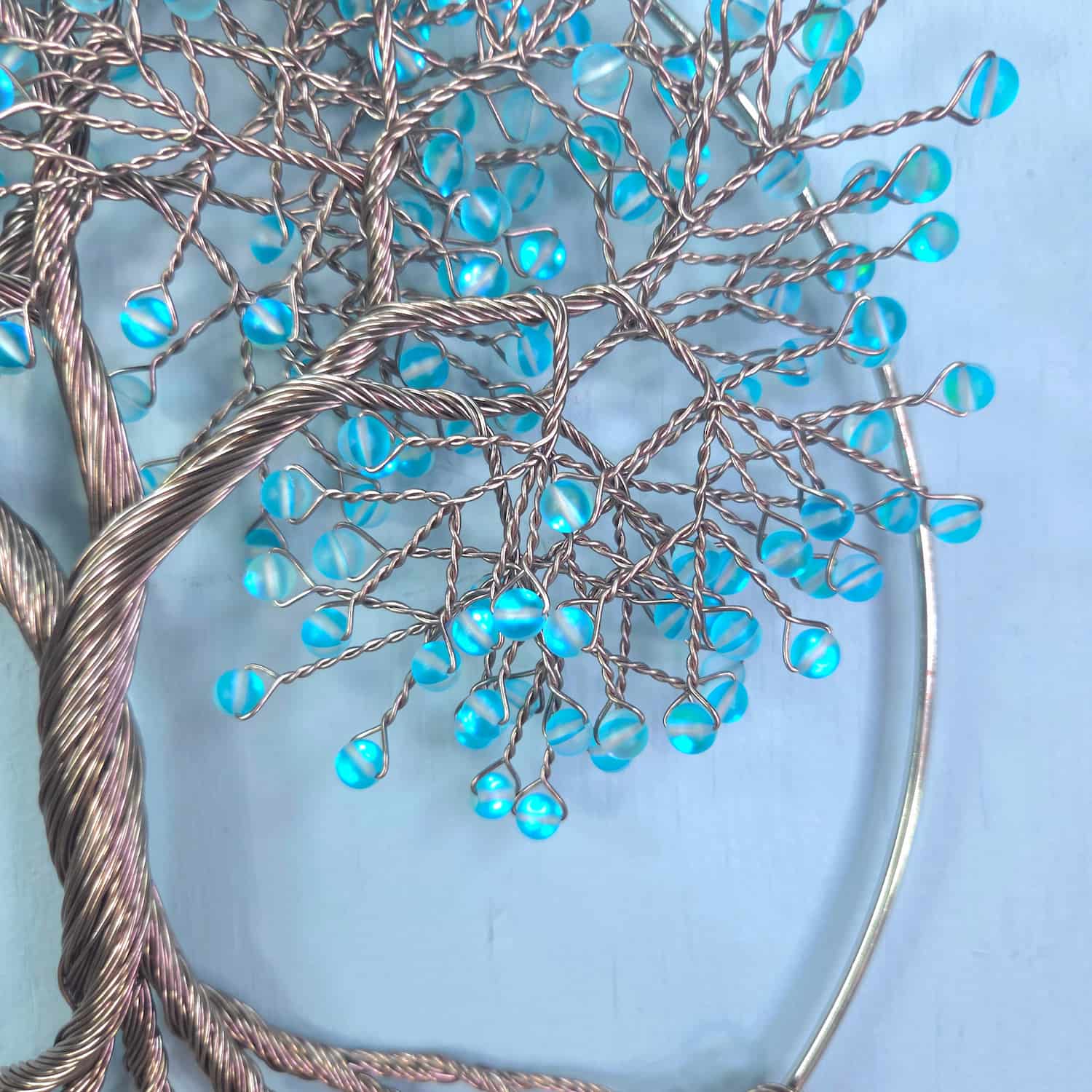 A decorative wire tree of life wall hanging with metallic silver branches and small round blue glass beads, shown against a light blue background.