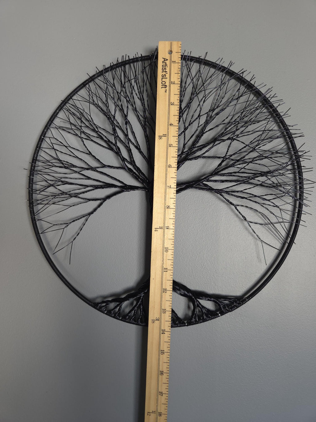 Decorative circular wall art with tree branches and a ruler for scale on a gray background