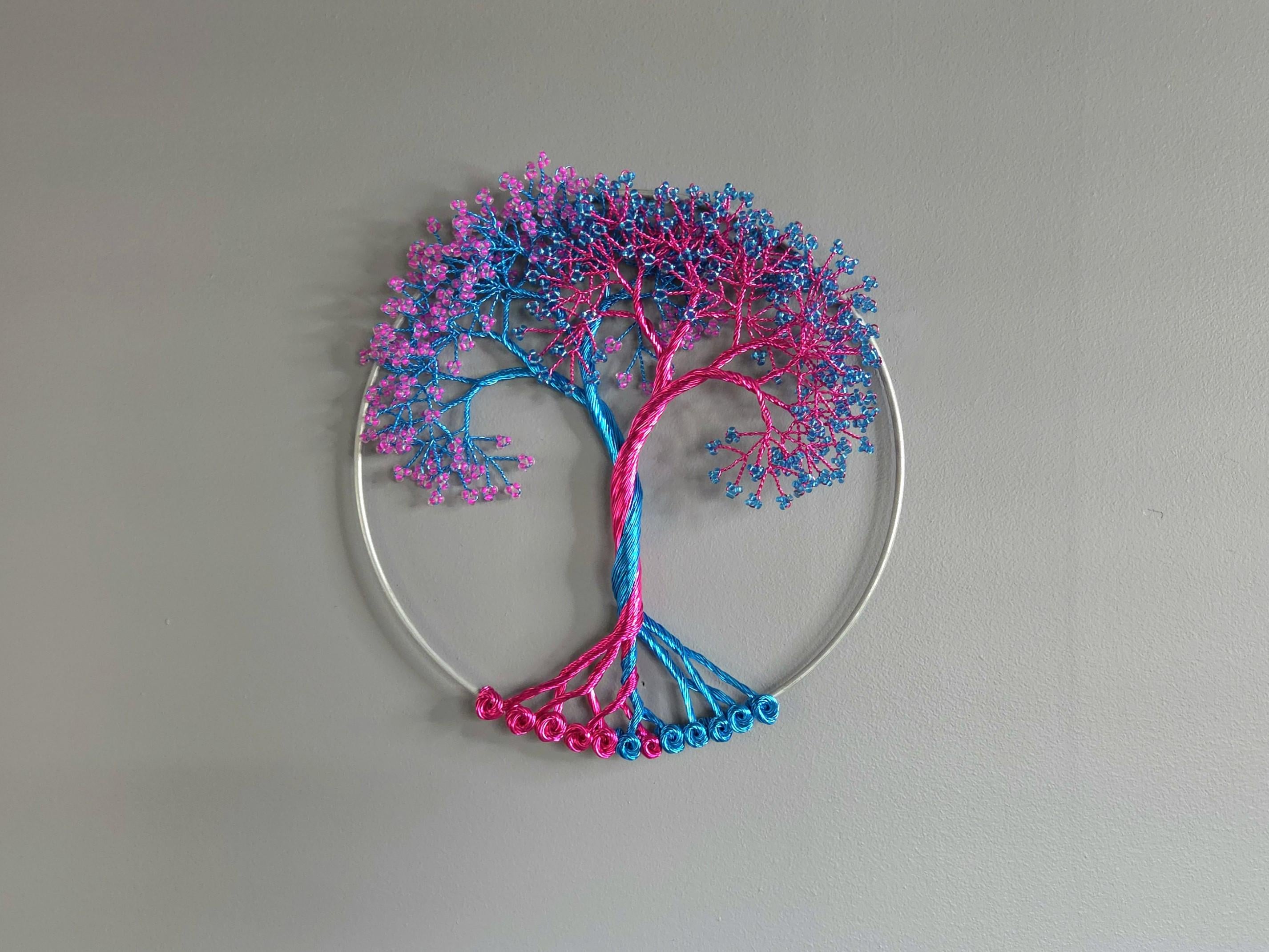 Decorative wall art in the shape of a tree with pink and blue branches on a gray background