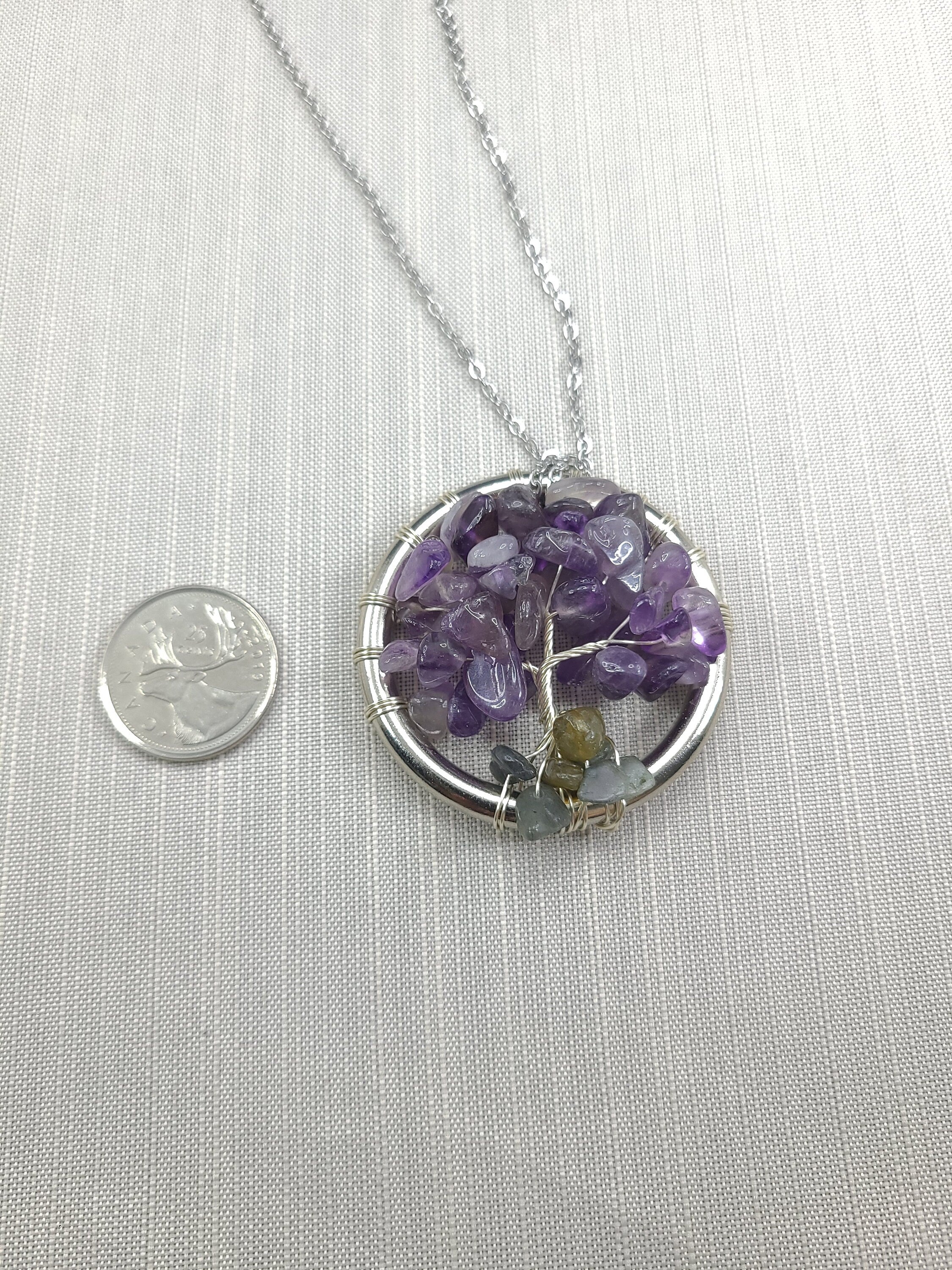 Necklace with a circular pendant featuring purple and green stones, next to a coin for scale on a white background.