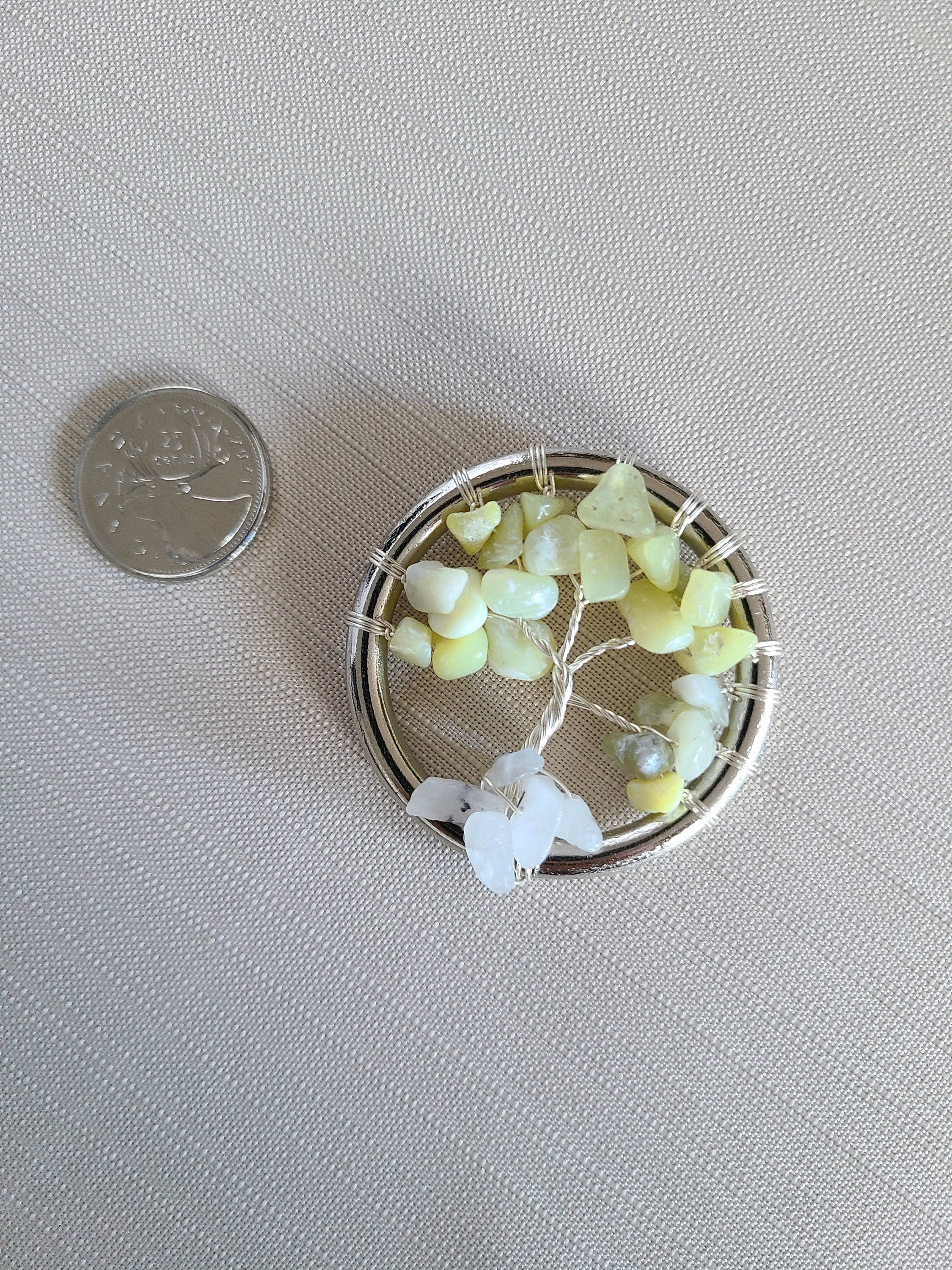 Small circular jewelry piece with green and white stones next to a coin on a gray background