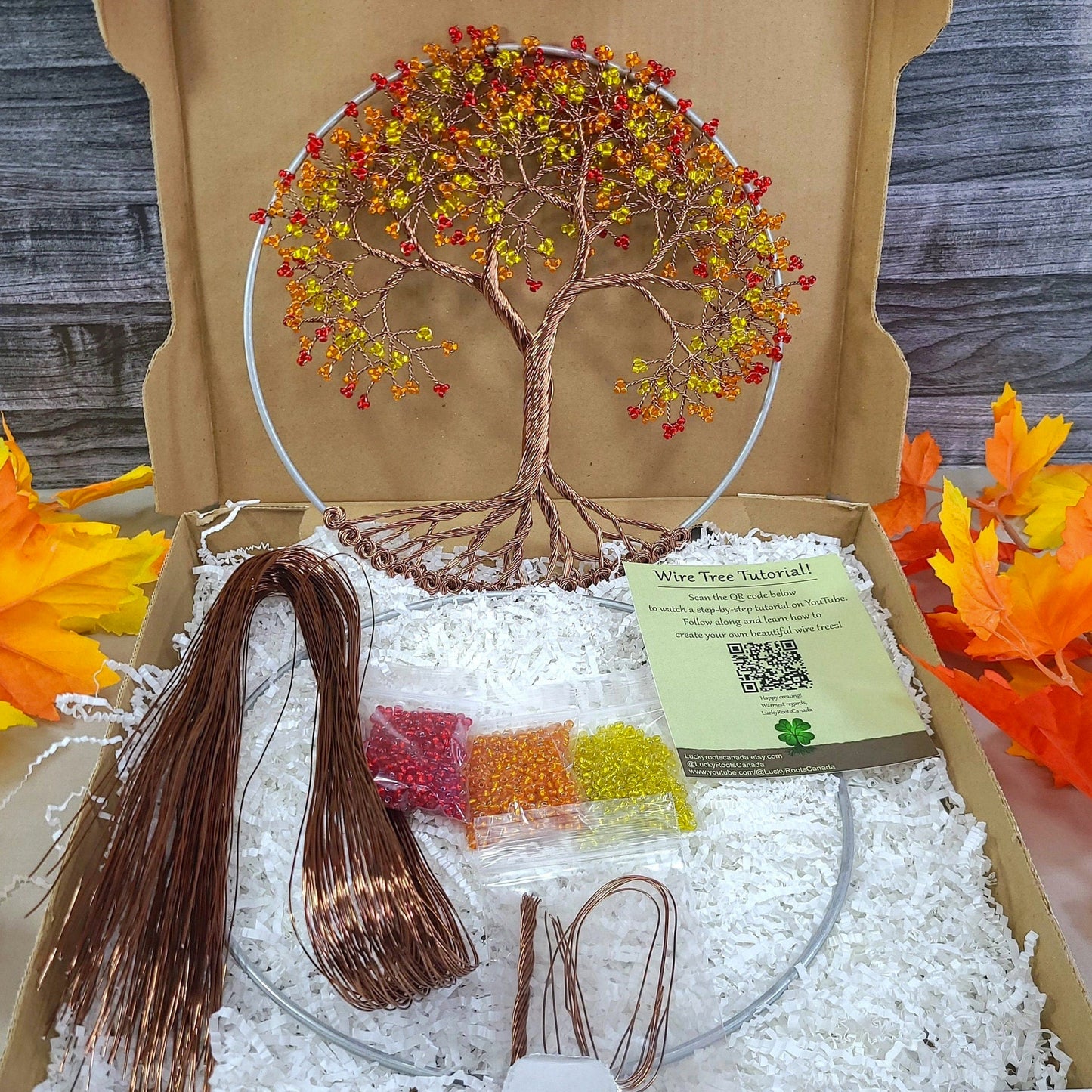 Craft kit with tree decoration and materials on a wooden surface with autumn leaves.