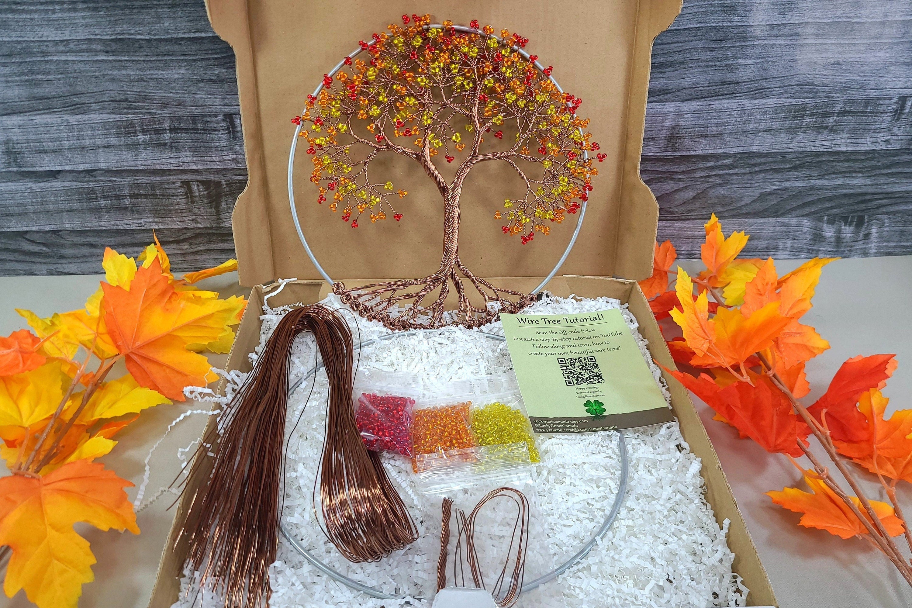 Craft kit with tree decoration and materials on a wooden surface with autumn leaves.