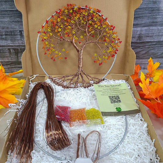 Craft kit with tree decoration and materials on a wooden surface with autumn leaves.