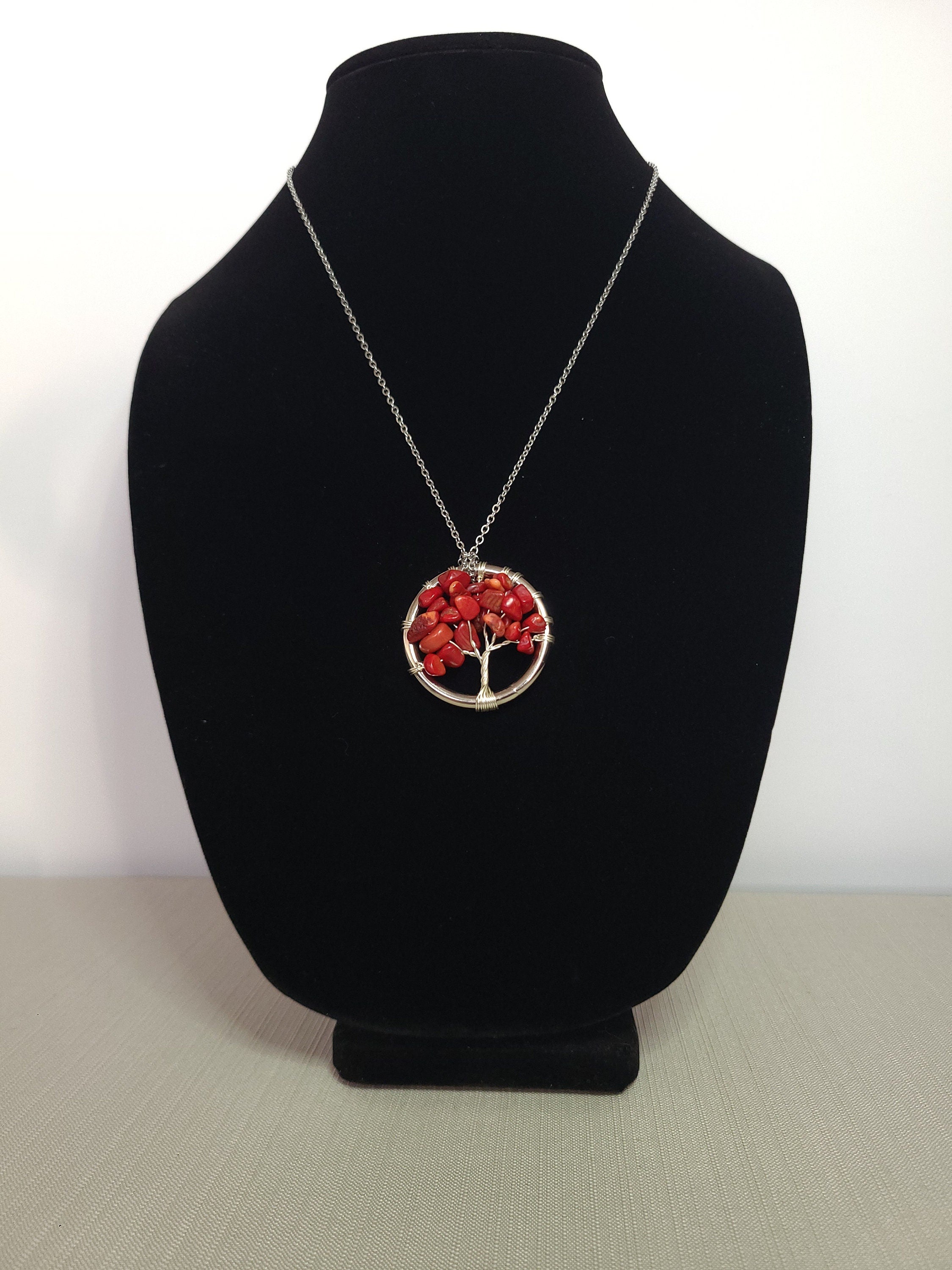 Necklace with a red tree pendant on a black bust against a white background