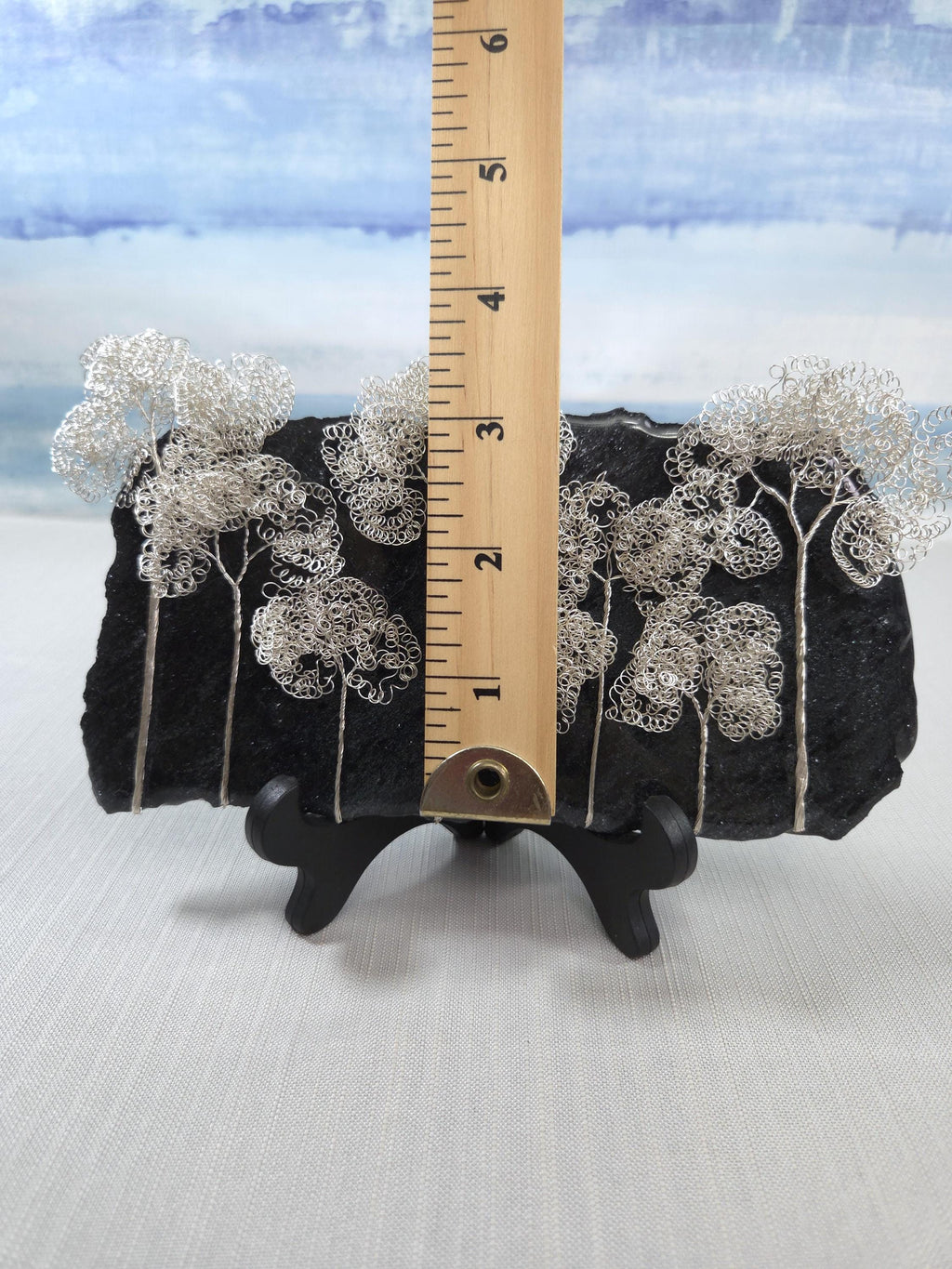 Decorative black rock with silver tree designs and a ruler for scale on a white background