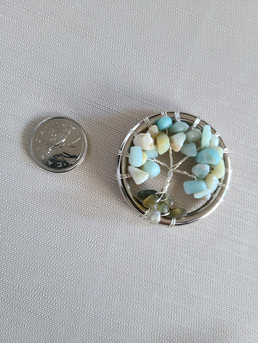 Small circular decorative item with stones next to a quarter on a light gray background