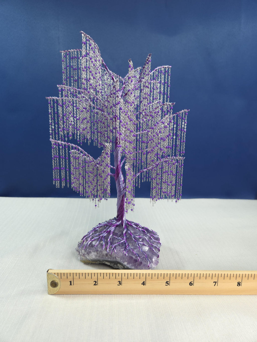 Decorative purple tree sculpture on a white surface with a ruler for scale against a blue background
