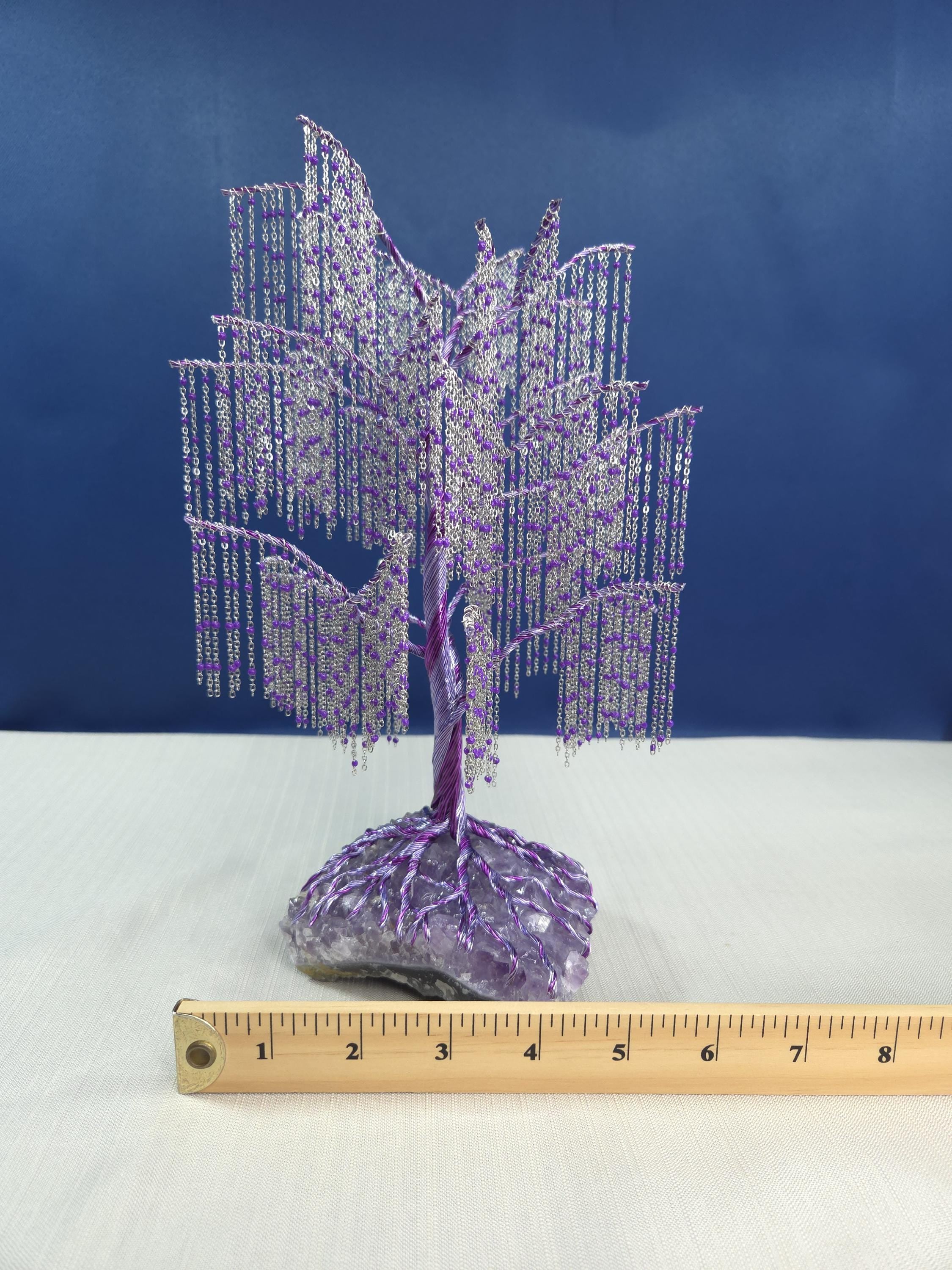 Decorative purple tree sculpture on a white surface with a ruler for scale against a blue background