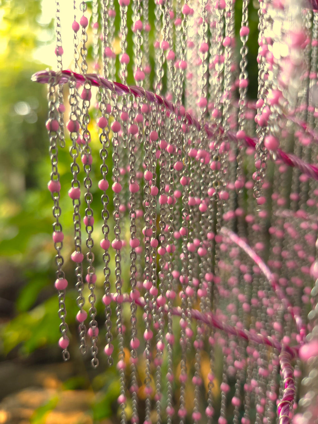 Pink bead curtain with blurred green foliage in the background