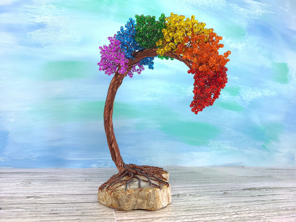 Colorful beaded tree with rainbow colors on a wooden base against a blurred natural background