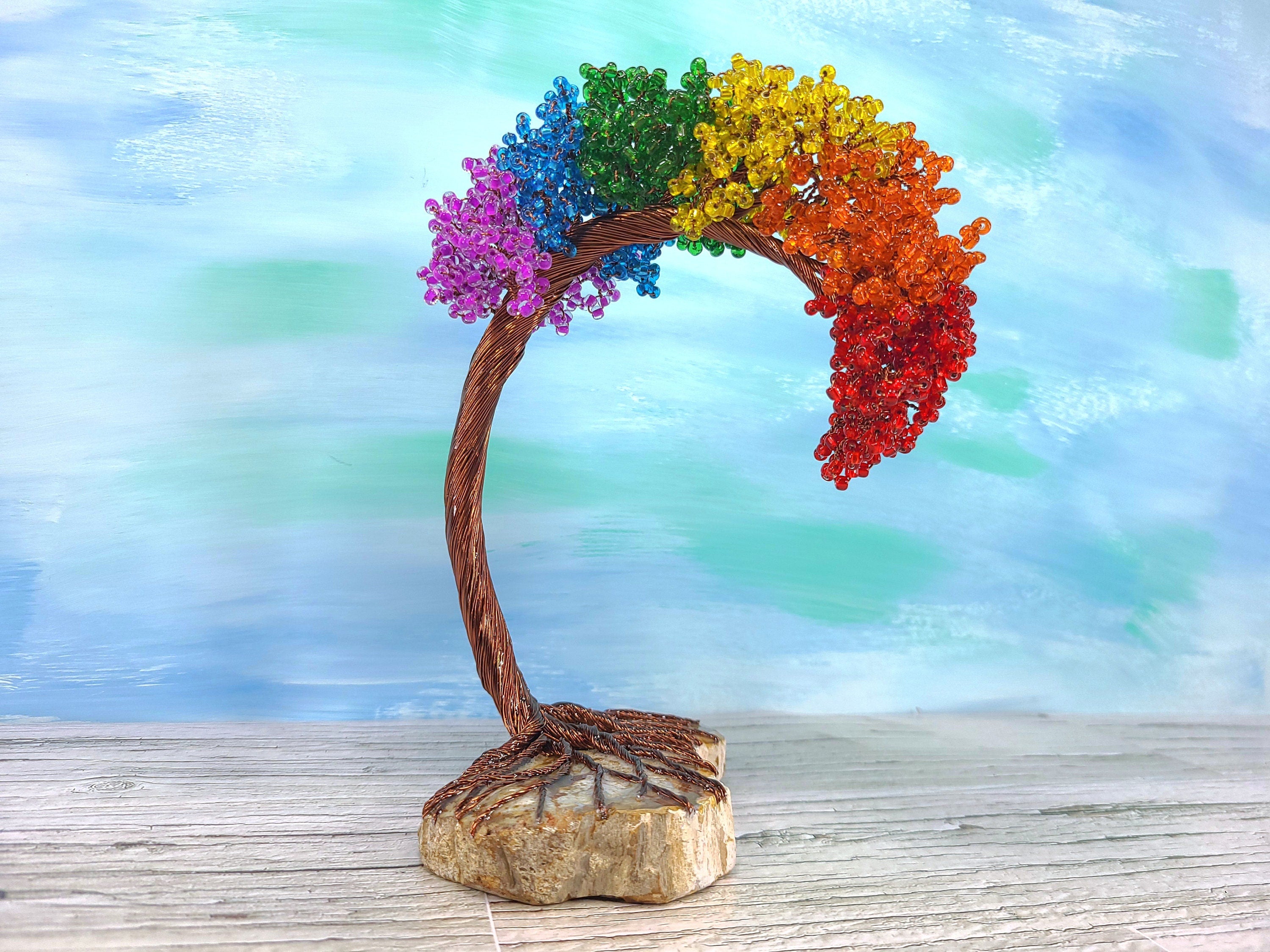 Colorful beaded tree with rainbow colors on a wooden base against a blurred natural background
