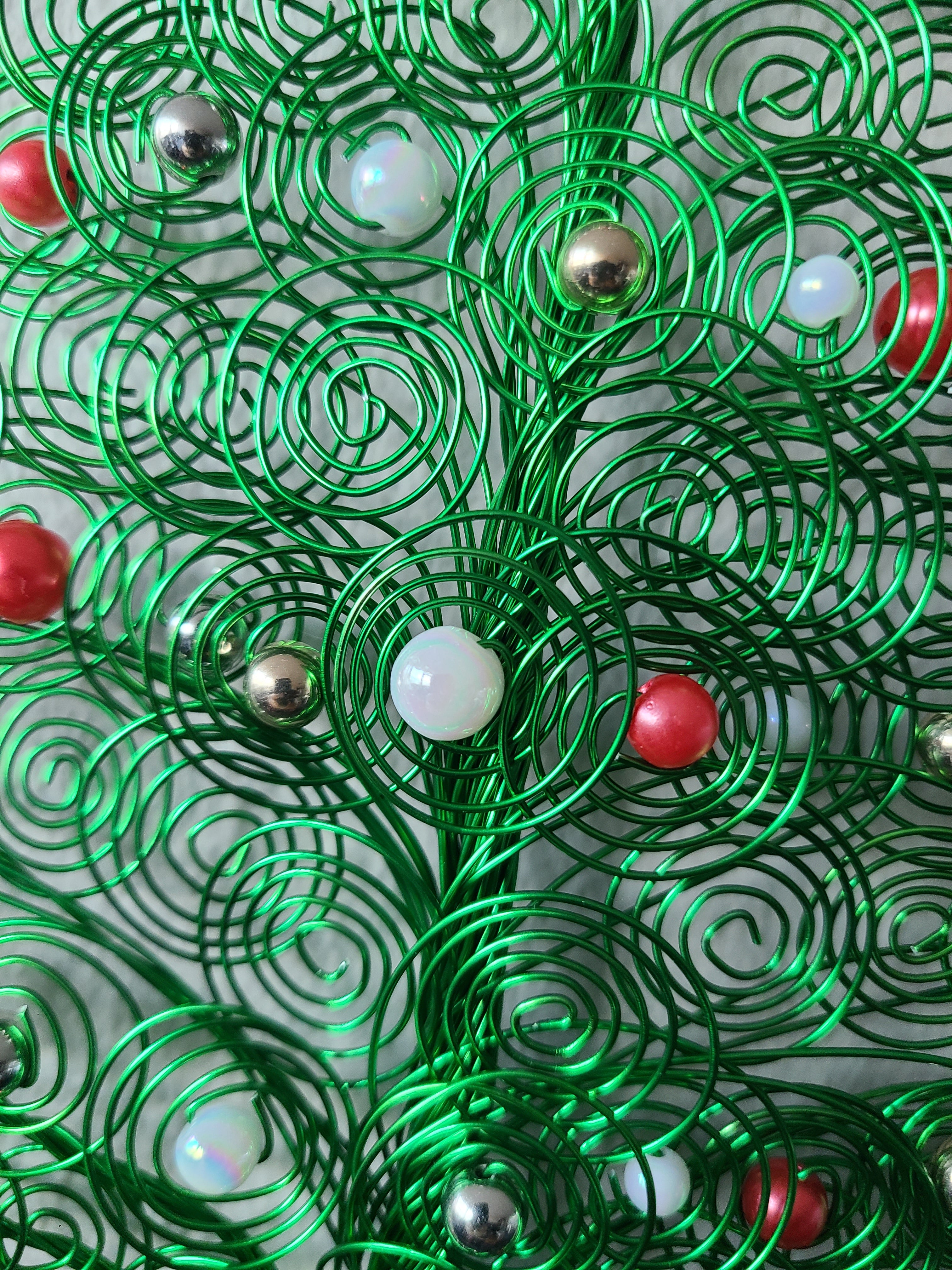 Green metallic spiral decorations with red and silver balls on a textured surface