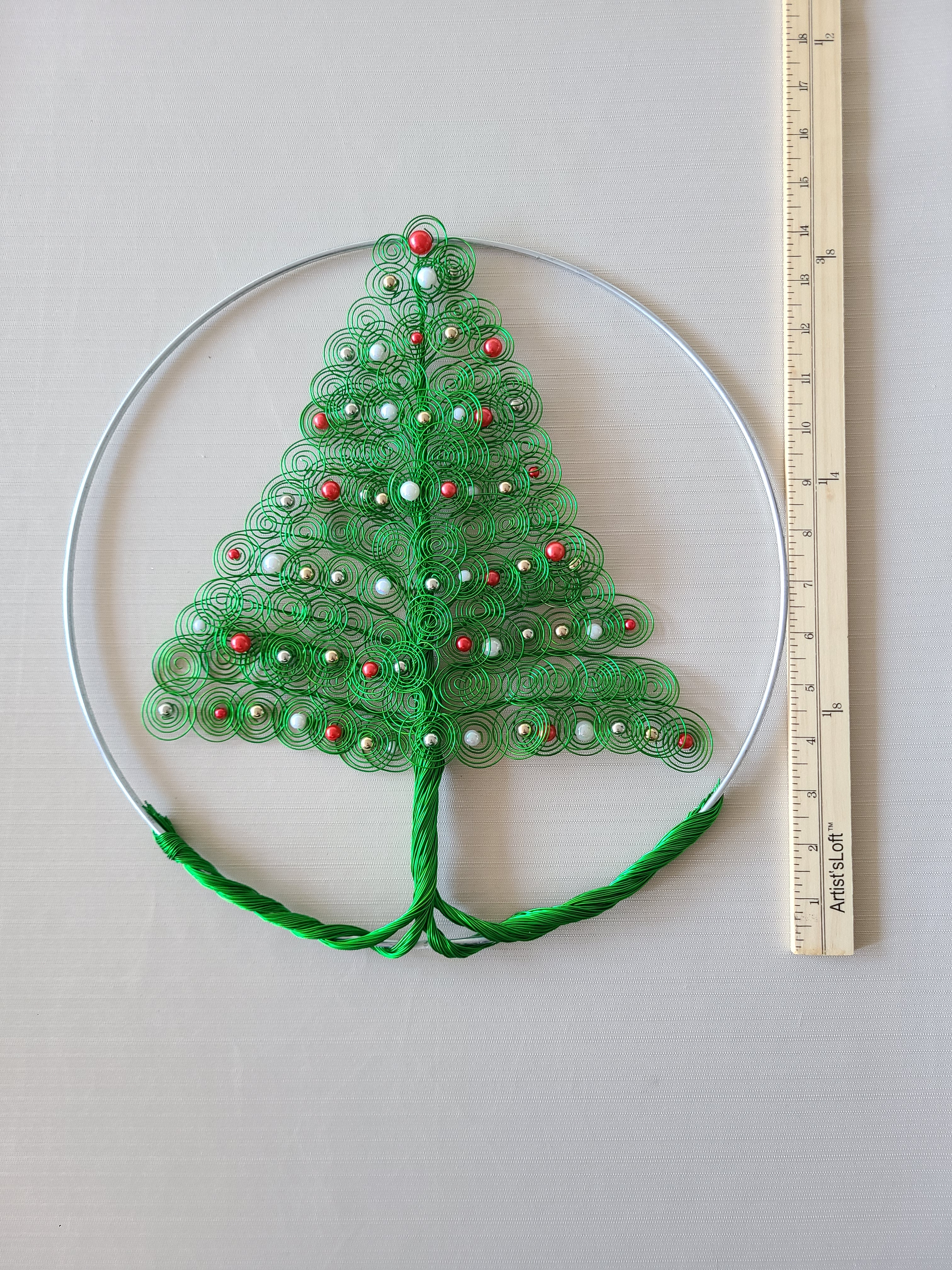 Green embroidered lace with red and white beads on a white background, measured by a ruler.