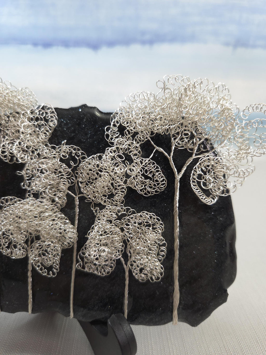 Silver wire tree sculpture on a dark stone surface with a blurred natural background