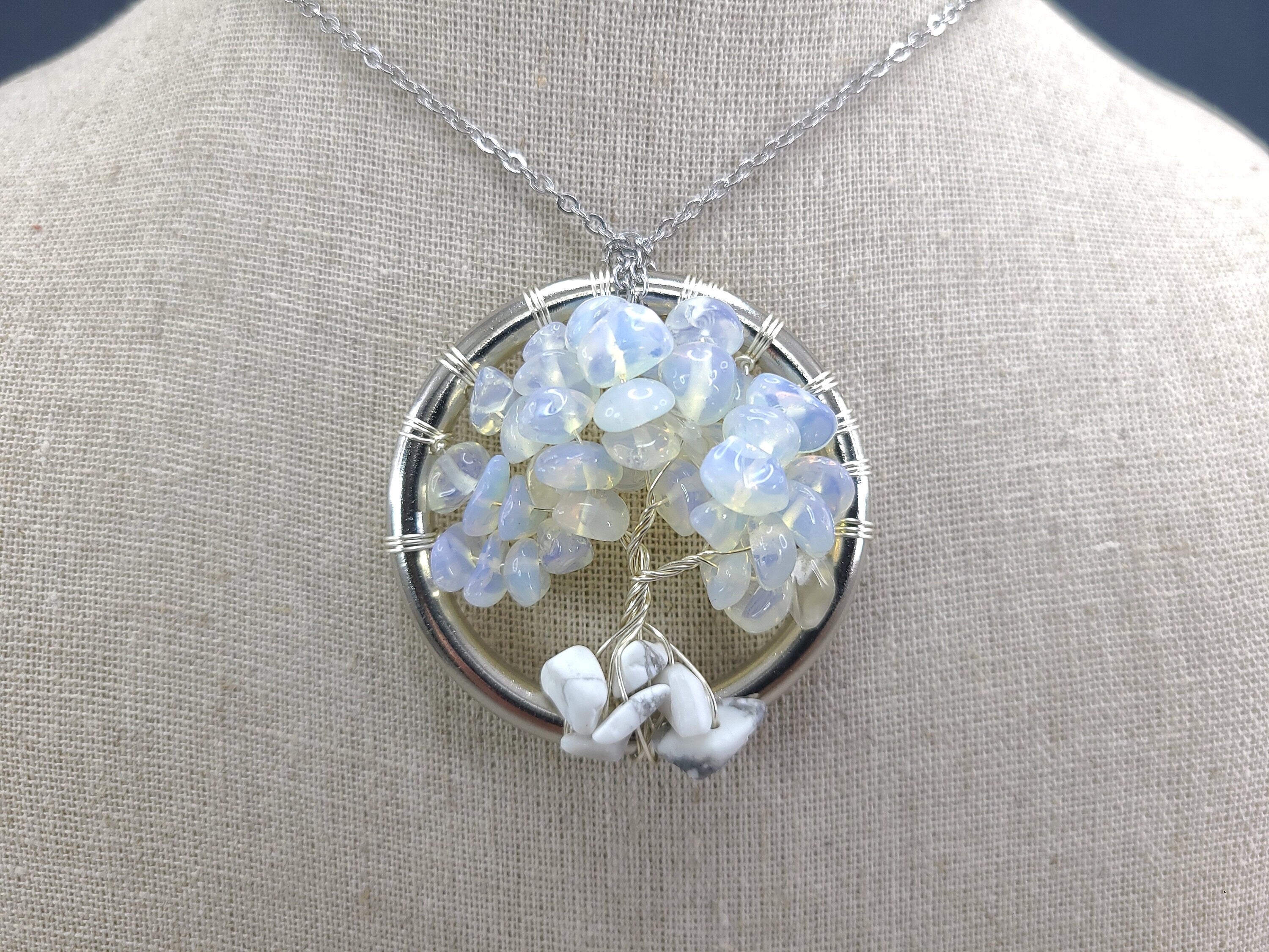 Silver necklace with a circular pendant featuring blue and white stones on a gray mannequin.
