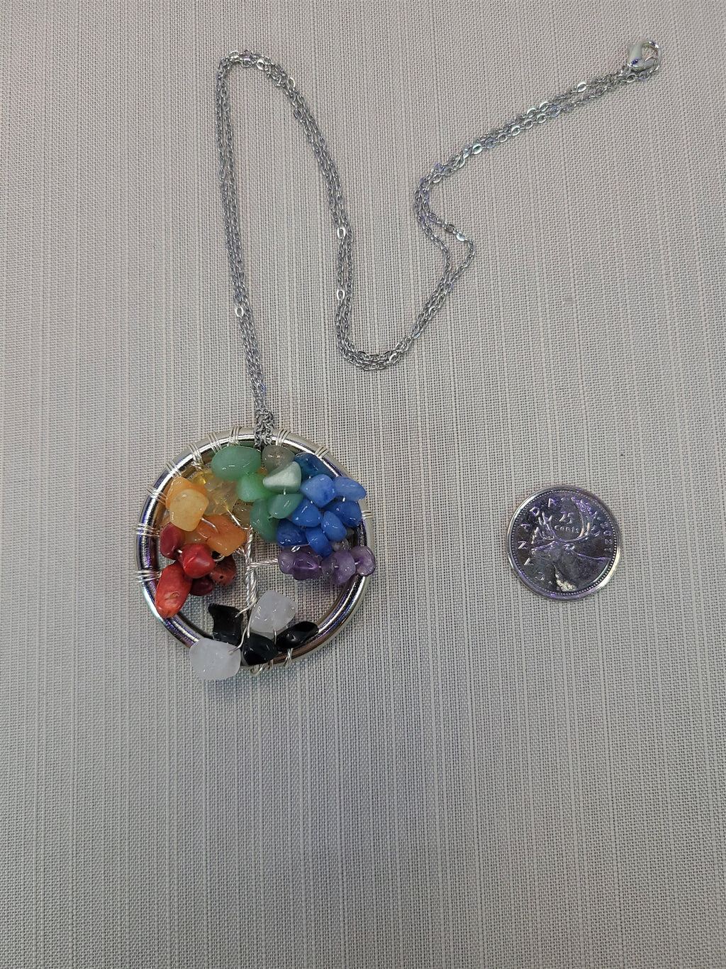 Colorful chakra pendant necklace on a chain with a quarter for scale on a gray background