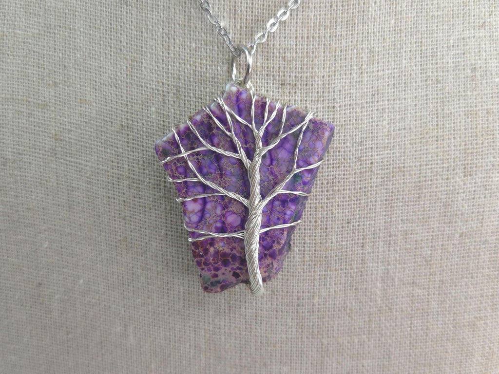 Purple stone pendant with silver tree design on a gray background