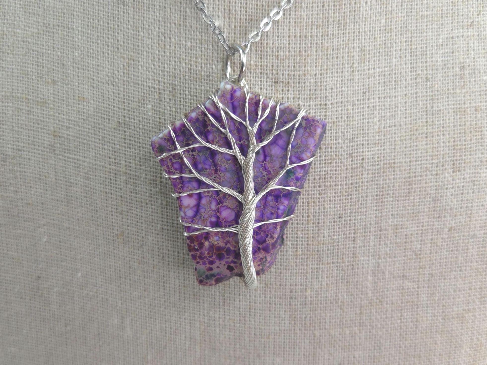 Purple stone pendant with silver tree design on a gray background
