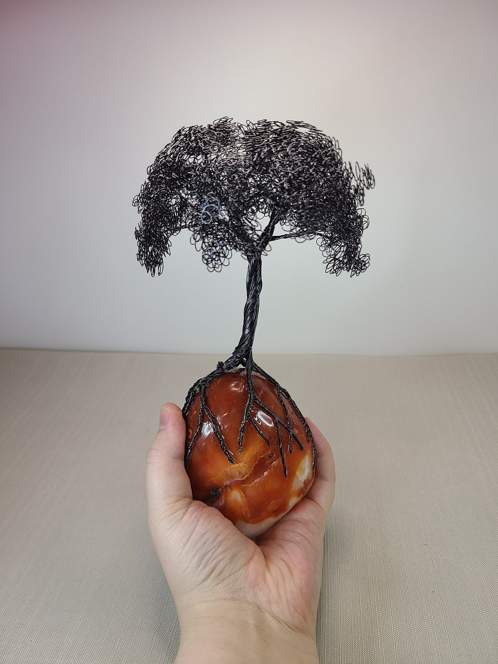 Hand holding a wire tree sculpture on a stone base against a plain background