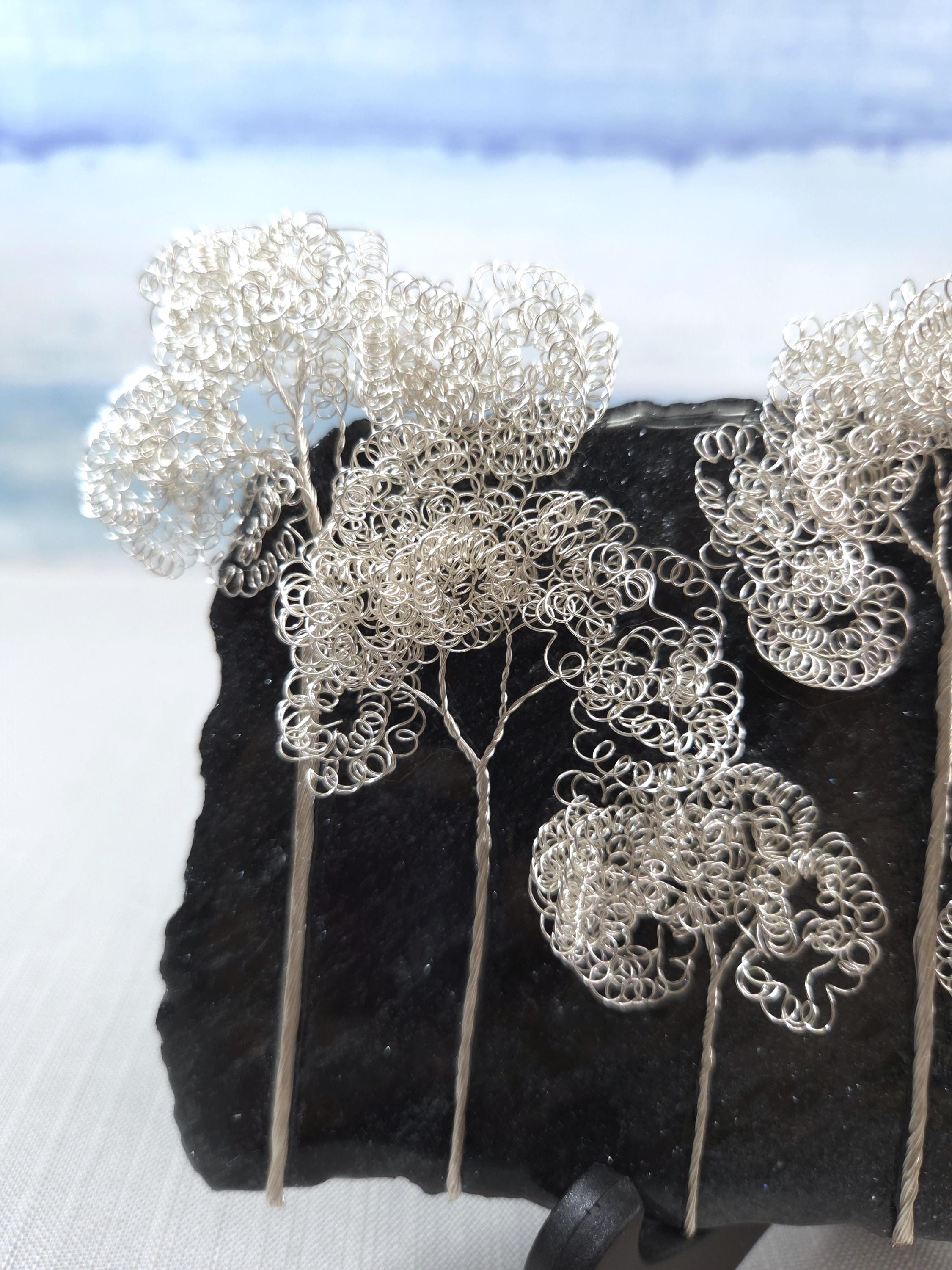 Silver wire tree sculptures on a black stone surface with a blurred natural background