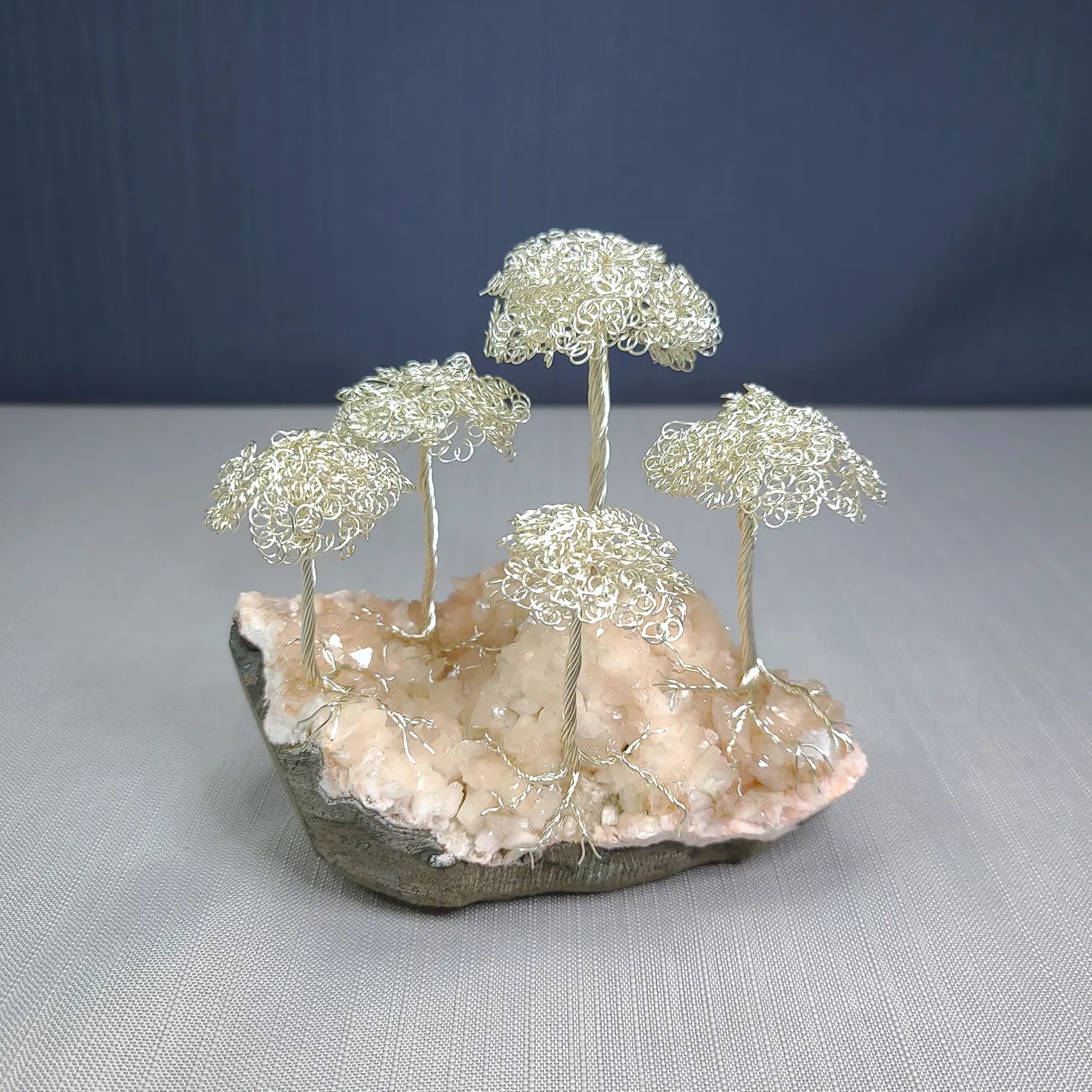 Decorative piece with wire trees on a rock base against a gray background