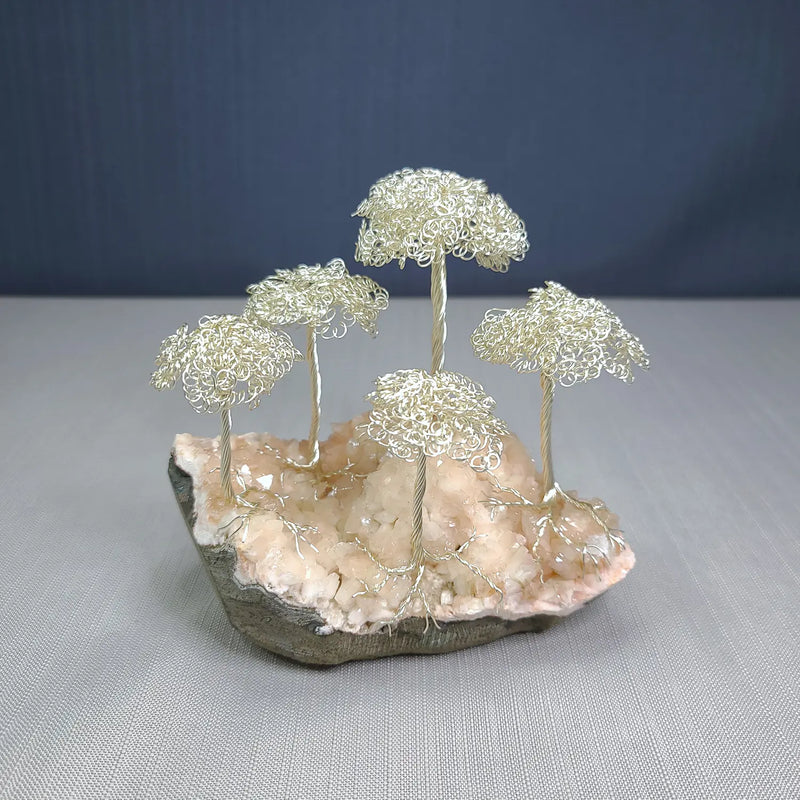 Decorative piece with wire trees on a rock base against a gray background